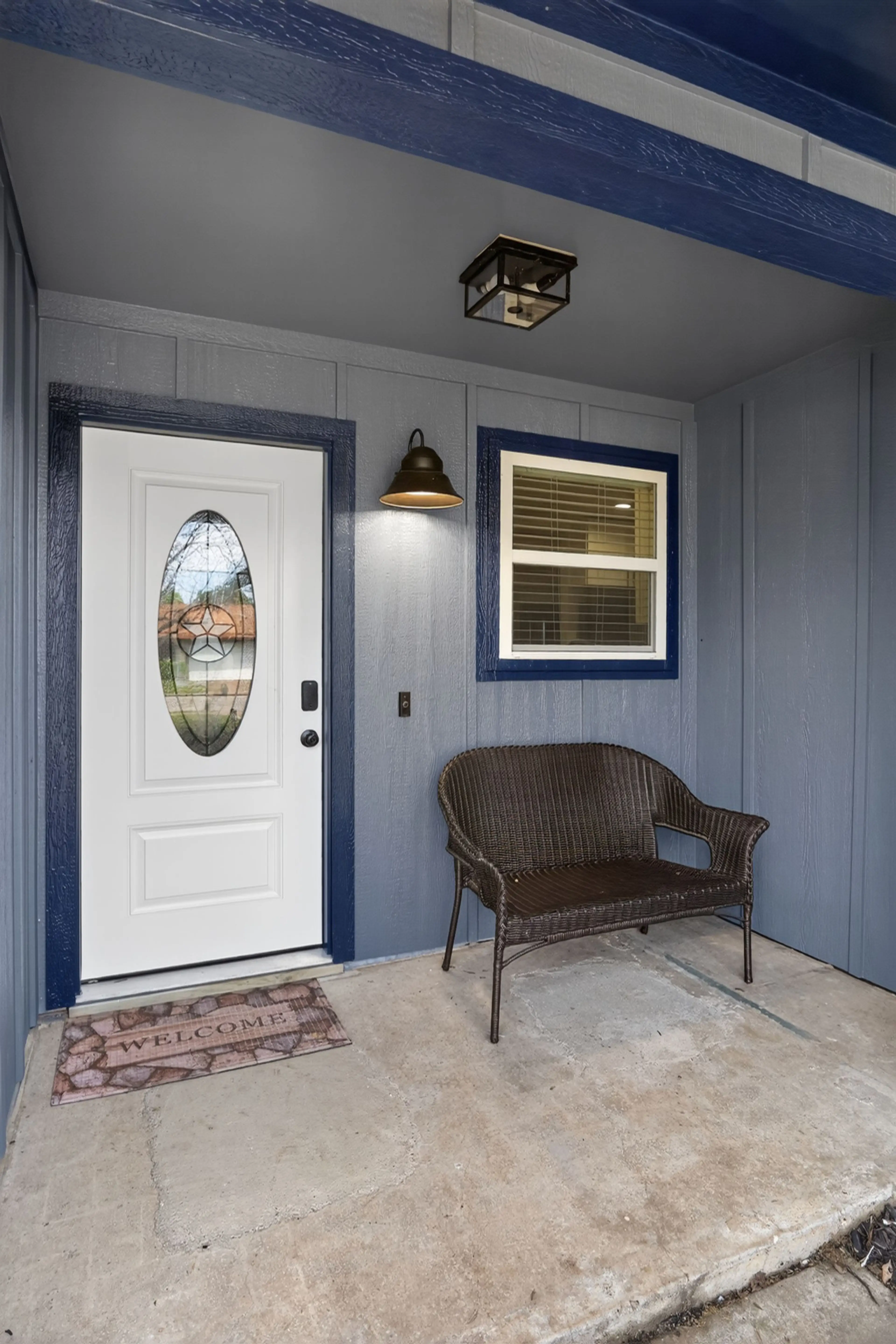Welcoming covered front porch with a beautiful Texas star stained-glass door, warm wall sconce, wicker loveseat bench, and a 'Welcome' mat — a charming first impression awaiting every guest in Irving, TX.