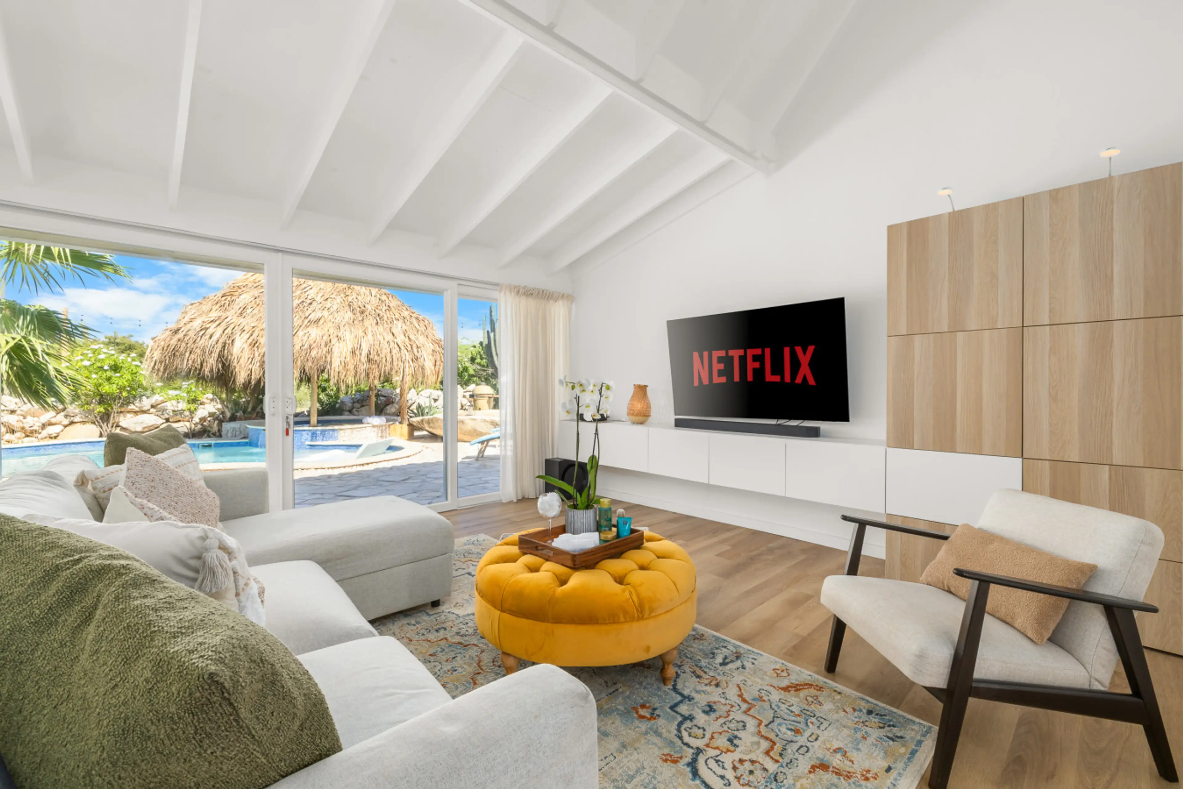 Bright, modern living room with sofa bed (comfortably sleeps 2 people), smart TV, and large sliding doors opening directly onto the pool and outdoor area