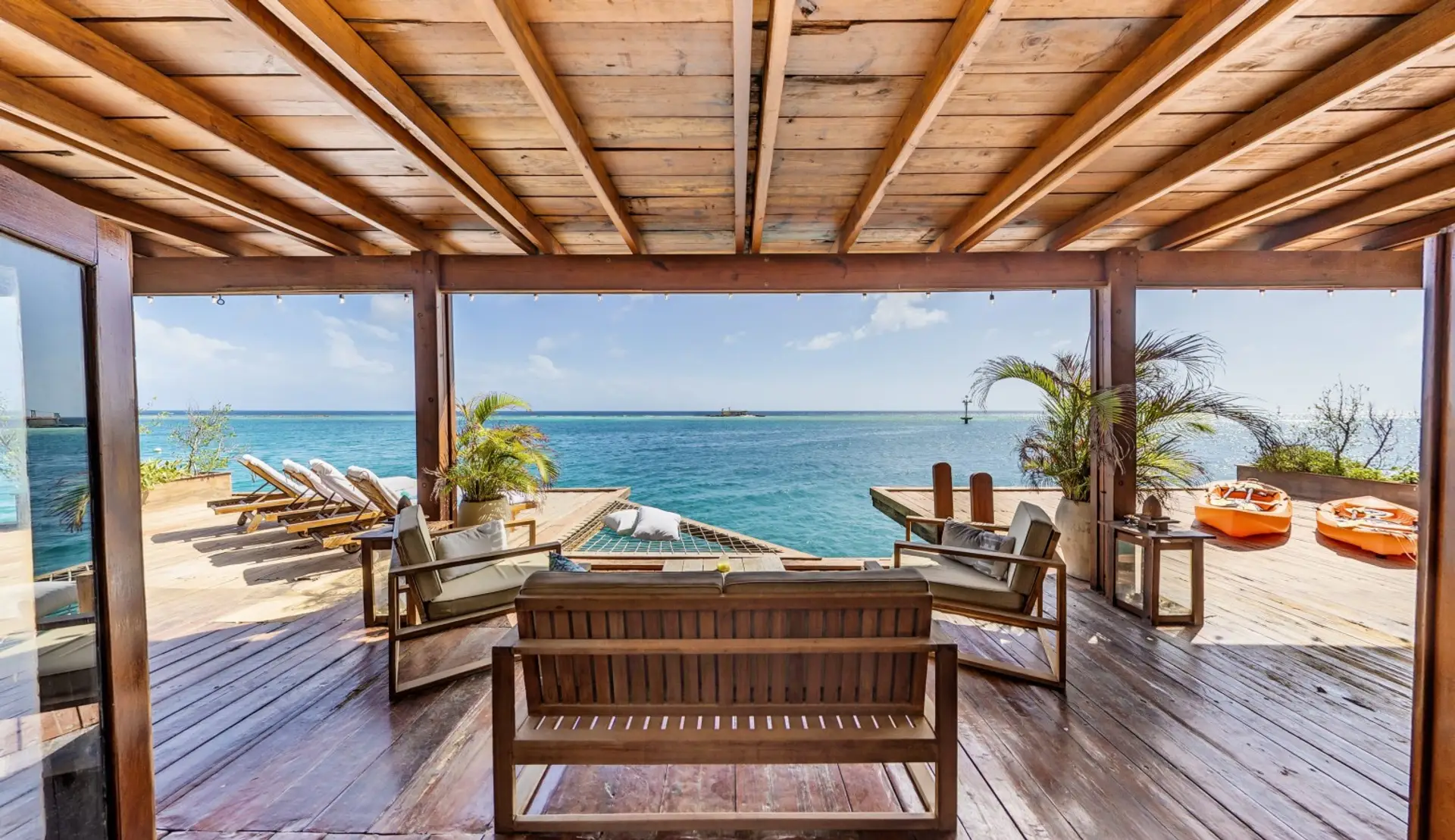 Oceanfront villa with overwater deck above clear turquoise sea, private wooden deck, sun loungers, outdoor seating, and direct access to the water. 100% solar powered.