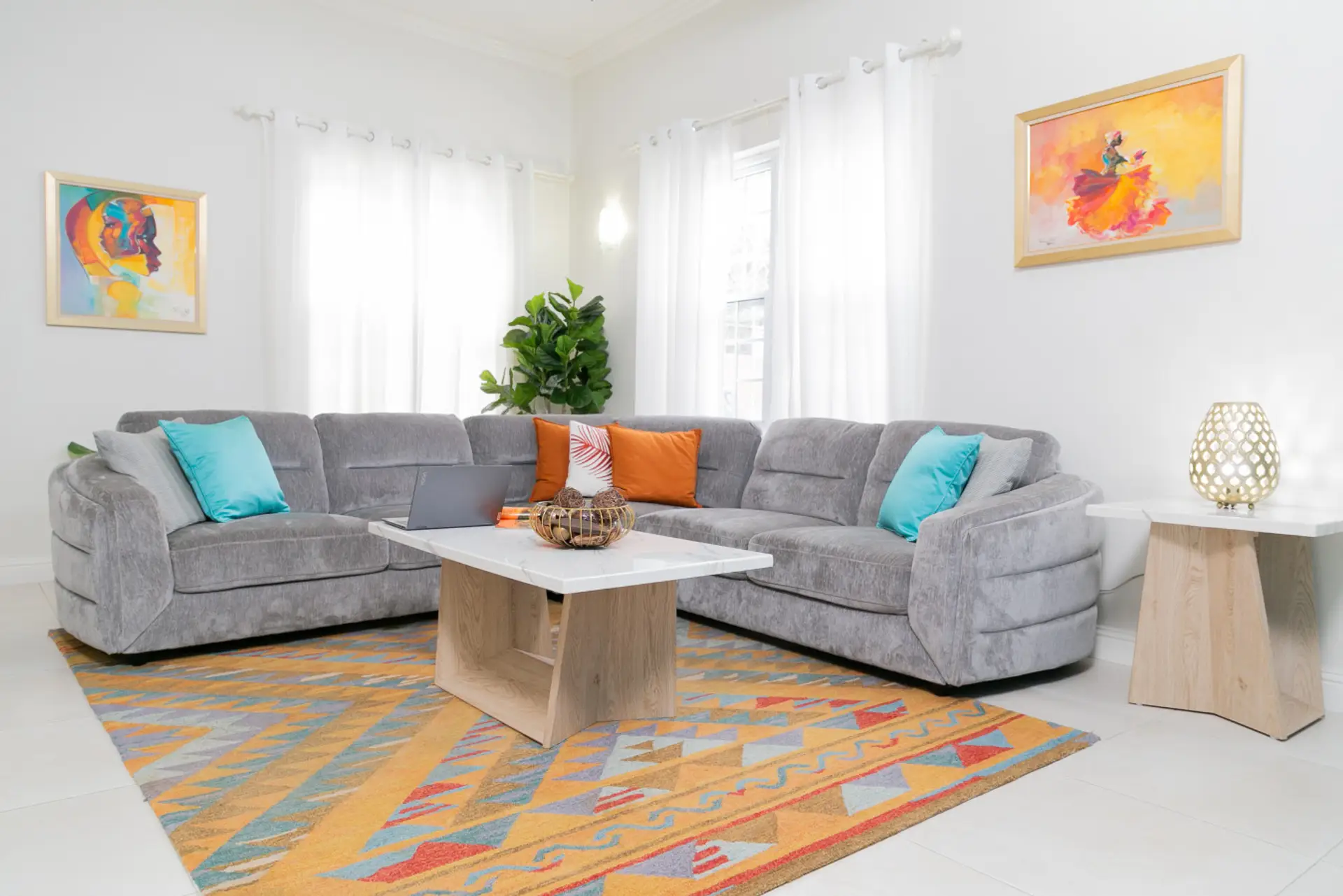 Bright living room w/ plush gray sectional, colorful rug & sunlit windows creating a cozy space to relax.
