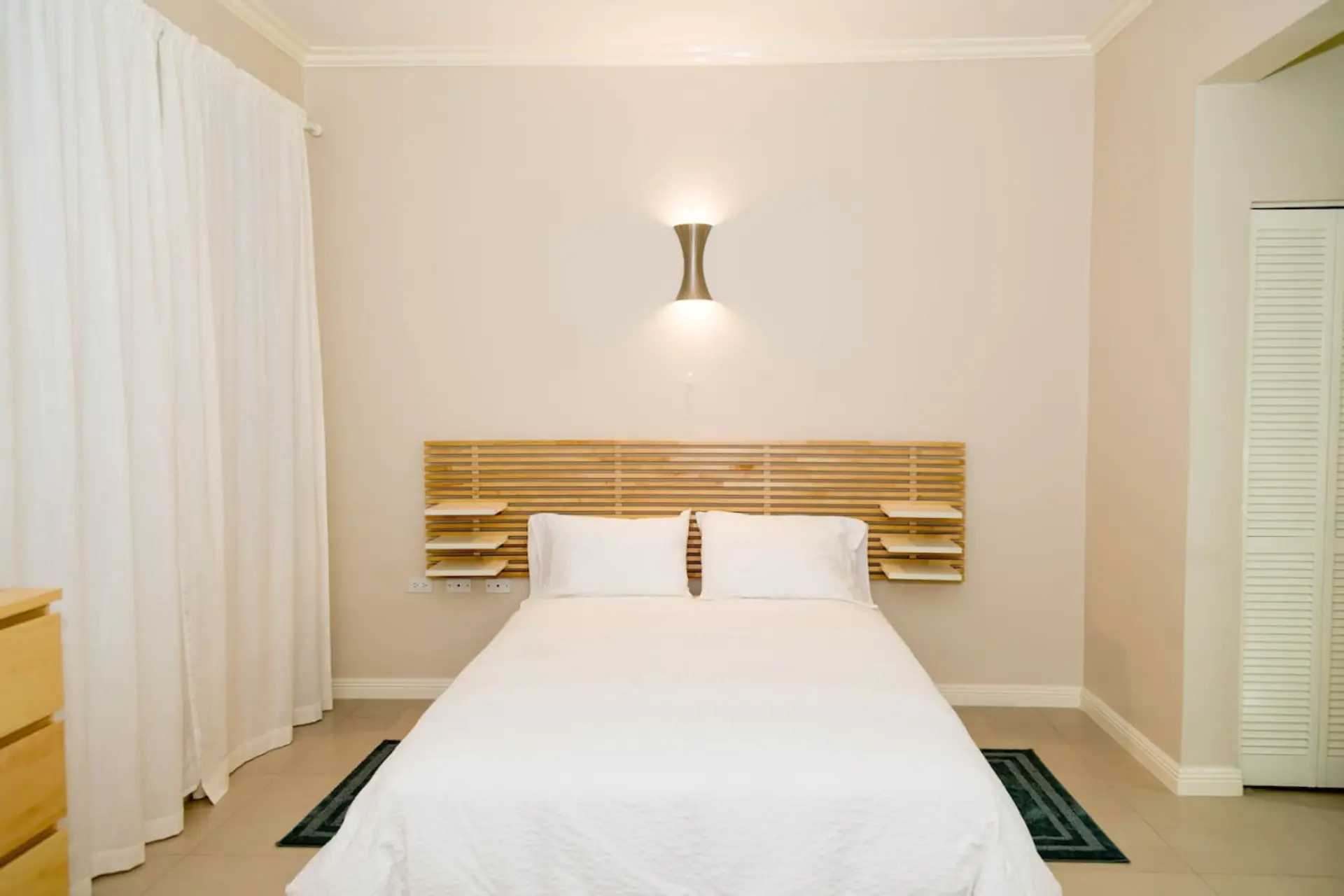 Simple, peaceful bedroom setup w/ a comfy bed, warm wall lighting & clean minimalist design for restful nights.