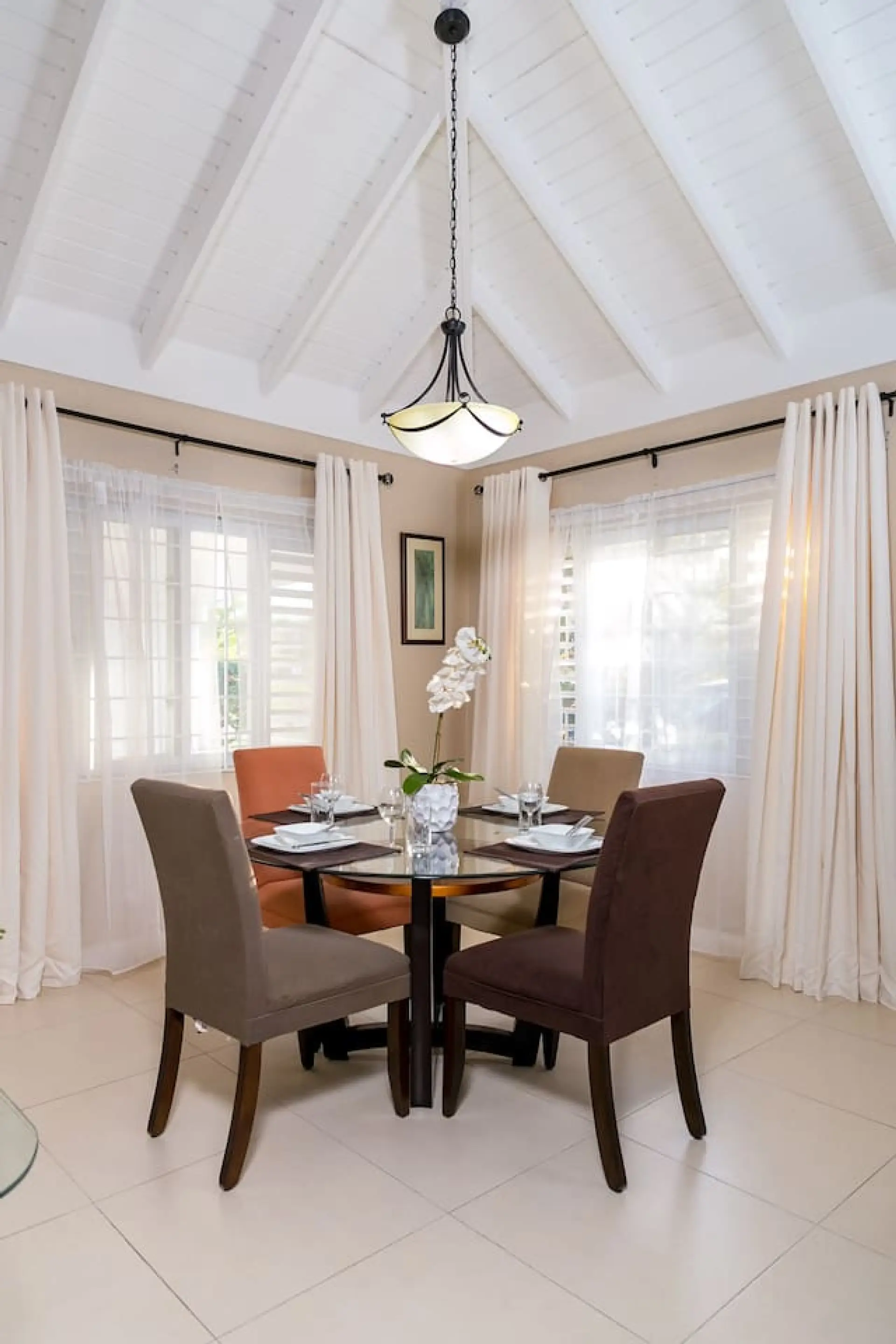Dining table set for a cozy meal beside tall windows draped in soft curtains