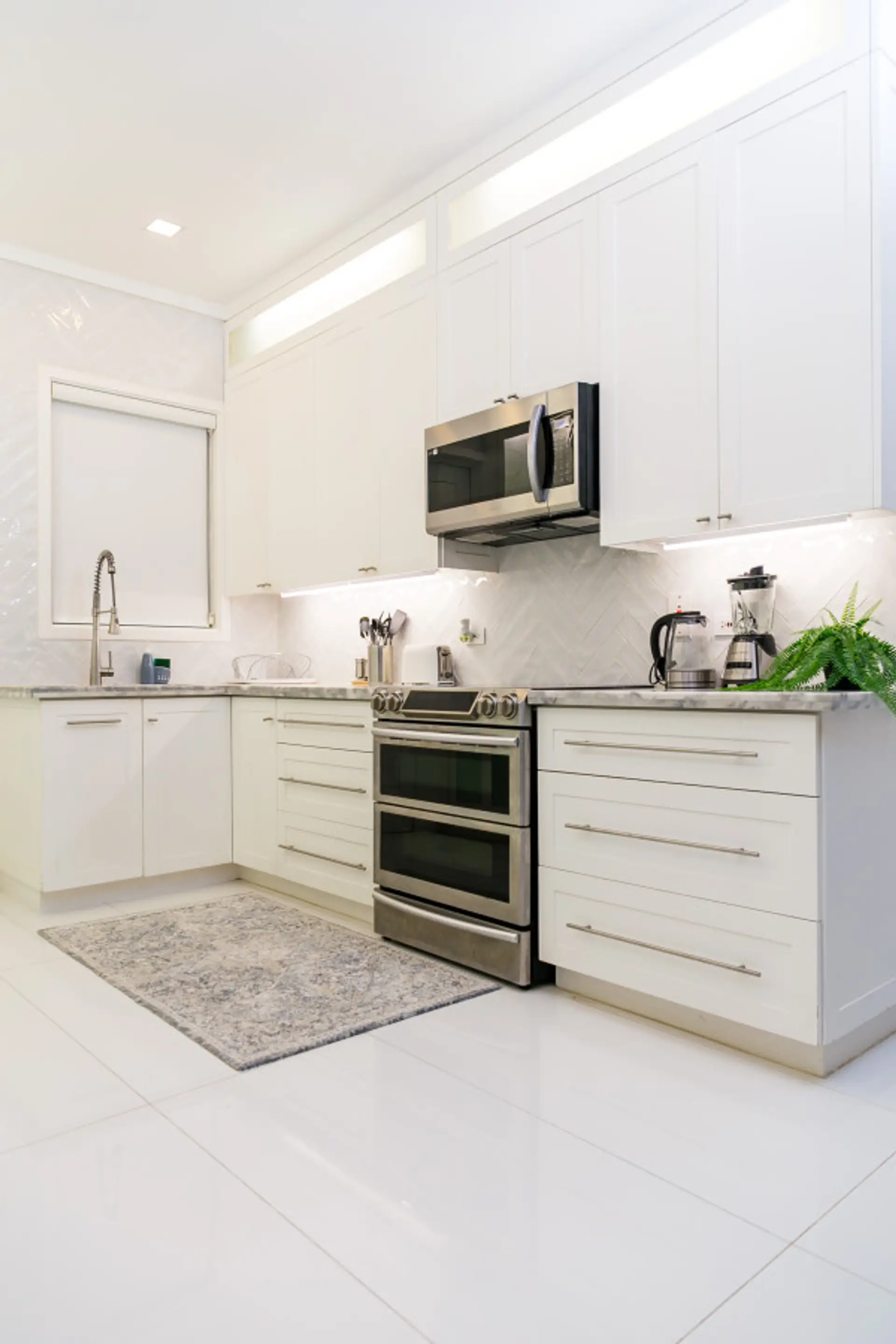 Sleek kitchen w/ white cabinets, stainless appliances & marble-style counters for easy meal prep