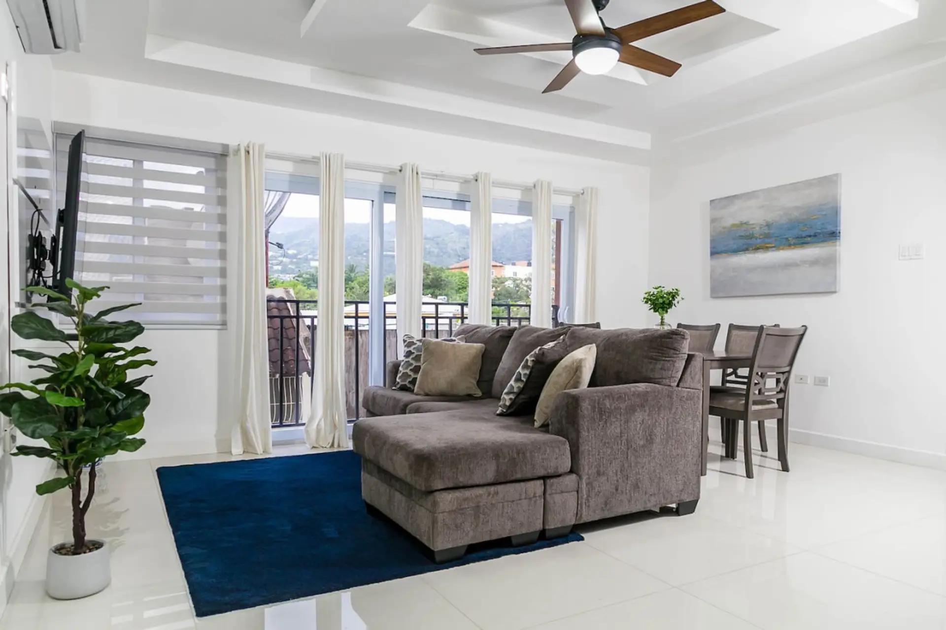 Bright living room w/ plush sofa, dining table & wall of windows letting in natural light