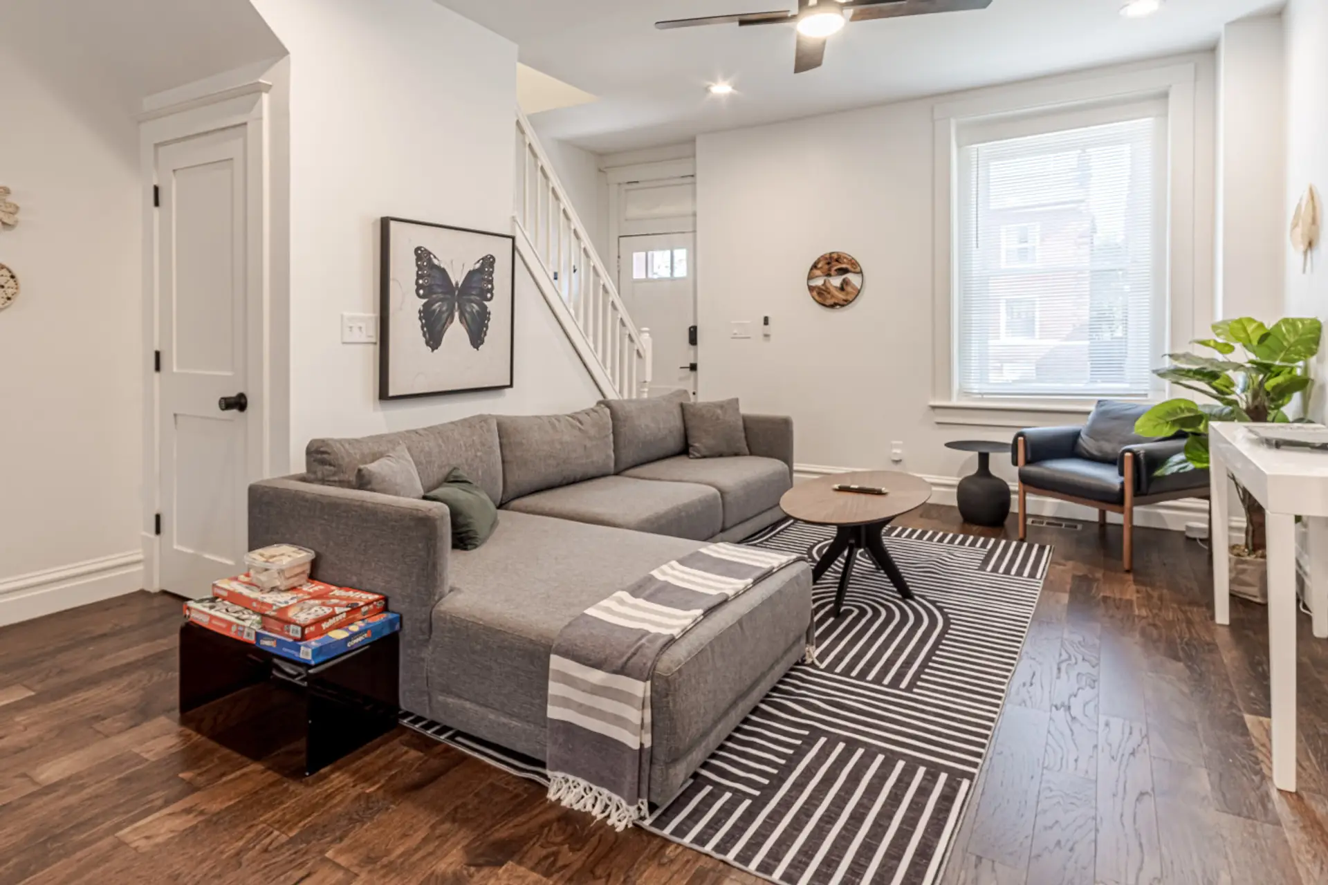 Open-Concept Living Area: Gather for cozy movie nights or family board games in this bright, open-concept living room outfitted with a spacious sectional sofa, modern area rug, hardwood flooring, and a dedicated staircase leading to the upper level.