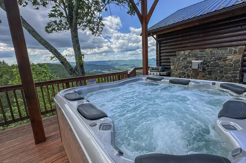 Private hot tub on the covered deck beside the stone fireplace and gas grill