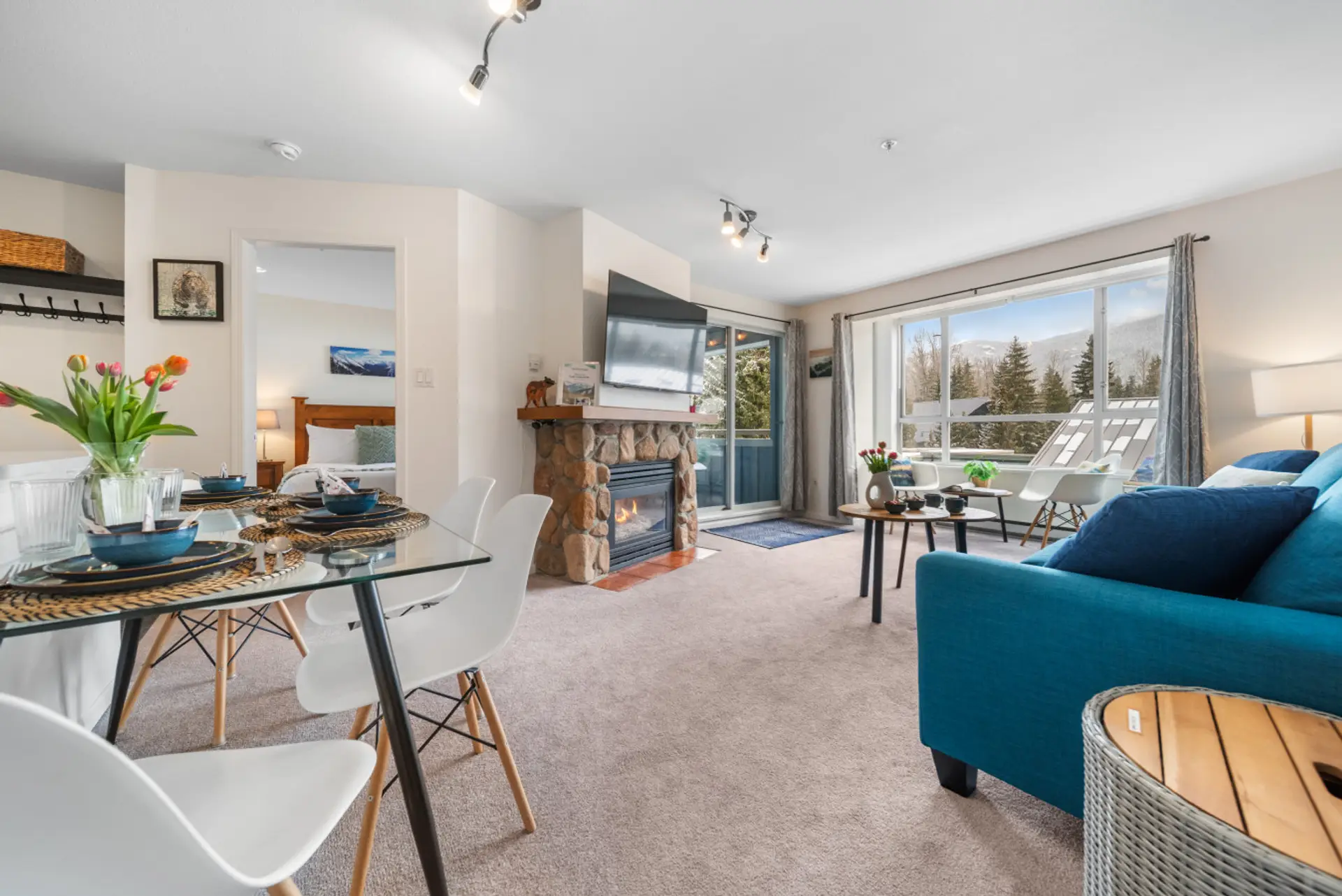 Bright open-concept living and dining area with fireplace, large windows, mountain views, and direct access to the balcony.
