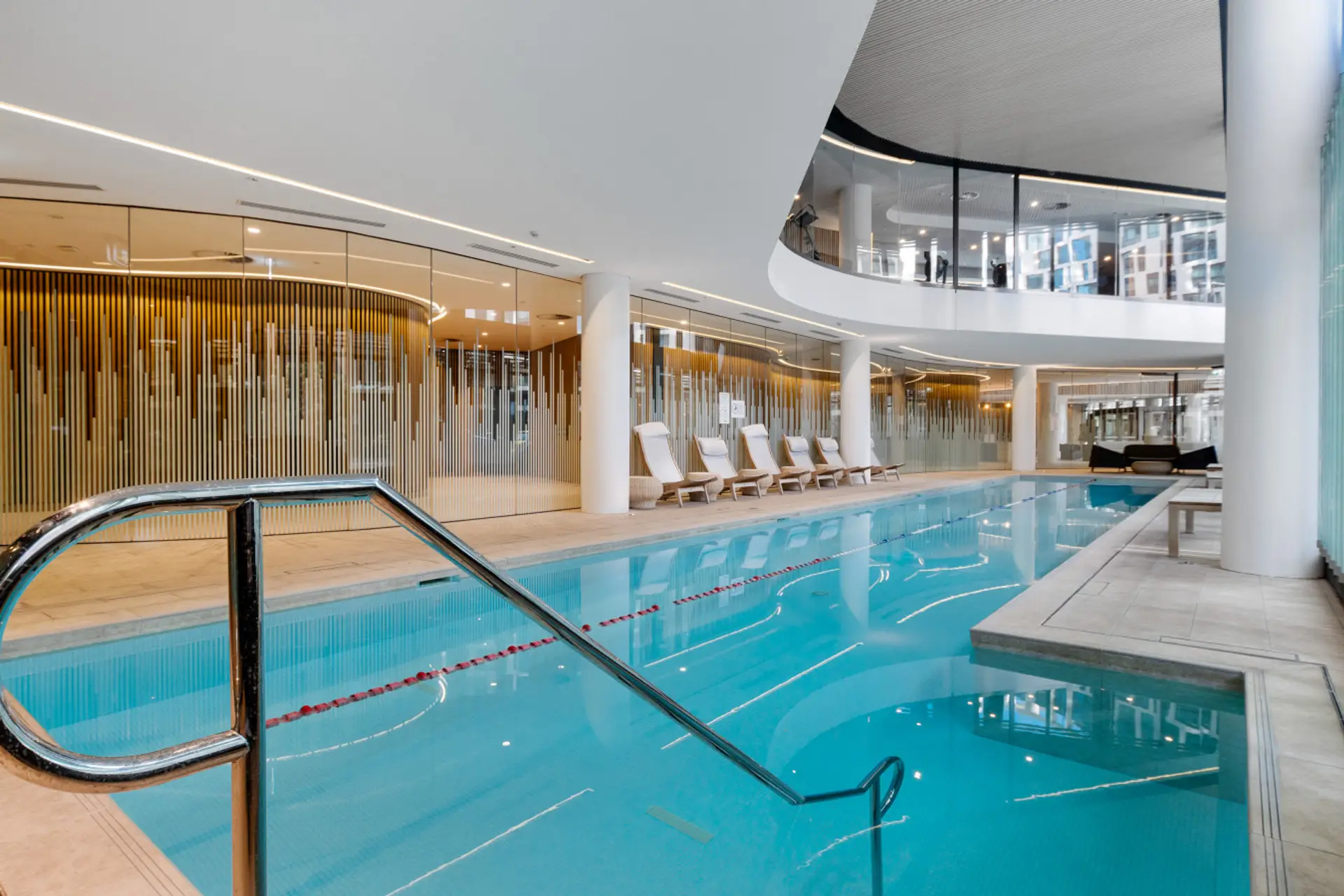 Indoor tepid lap pool on ground level with gym seen through glass windows on upper level 1.