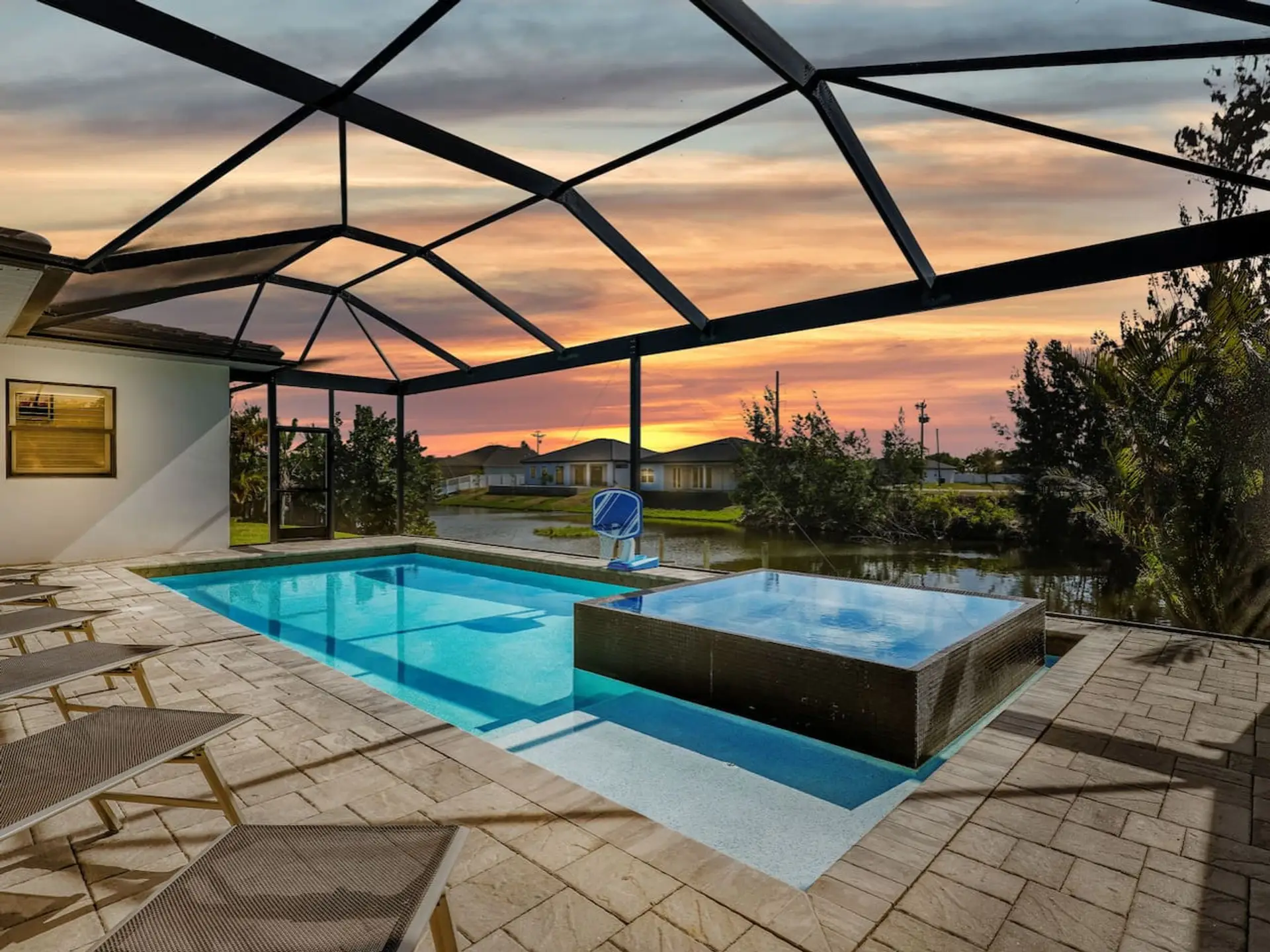 Unwind poolside at sunset in the screened lanai, featuring a private pool, spa, lounge seating, and waterfront views.