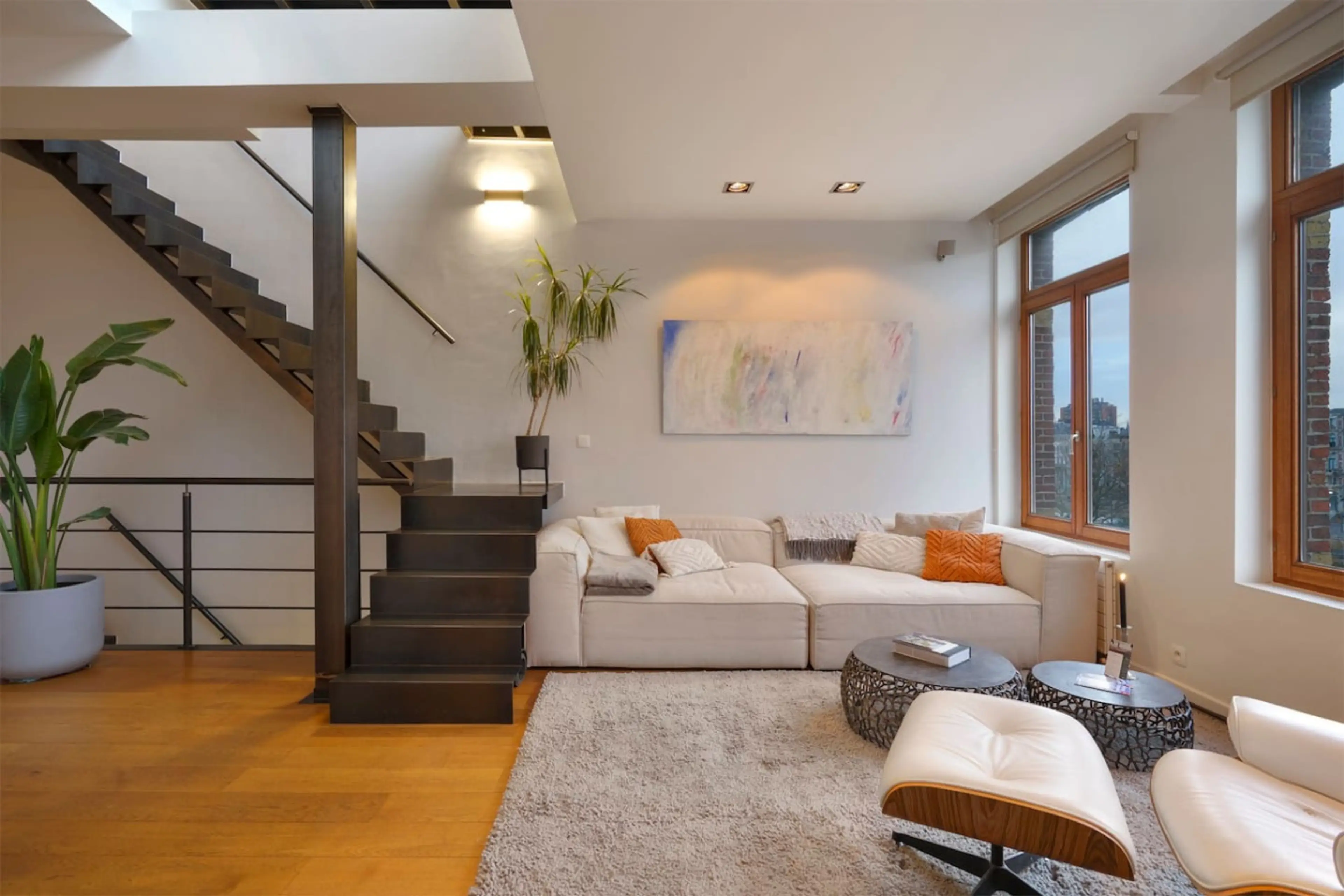 Bright living area w/ cozy sofa, warm lighting & stairs leading to an upper level