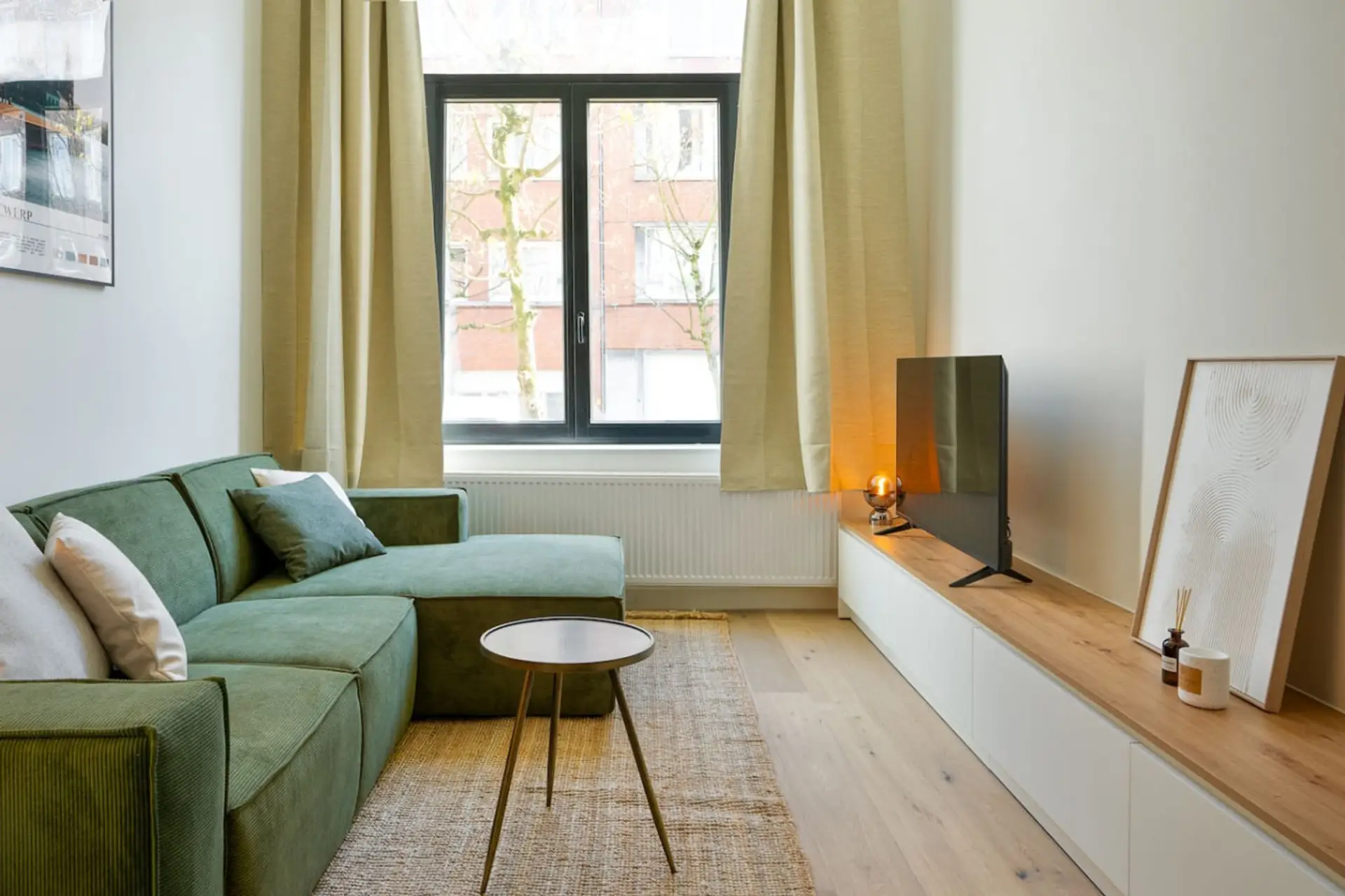 Sunlit living room w/ green sofa, wall-mounted TV & cozy seating by large windows