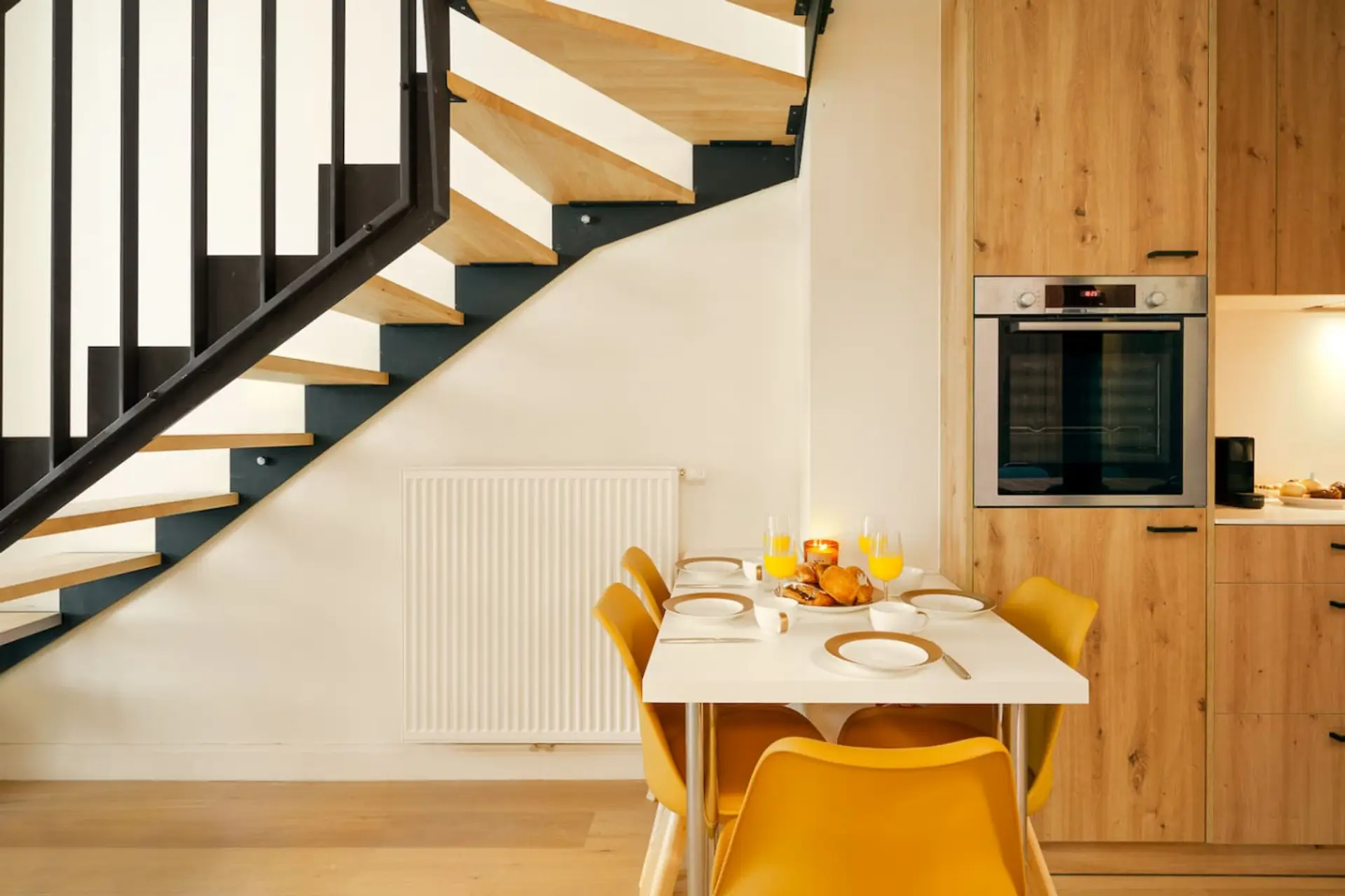 Bright dining nook beneath staircase flowing into a warm wood kitchen