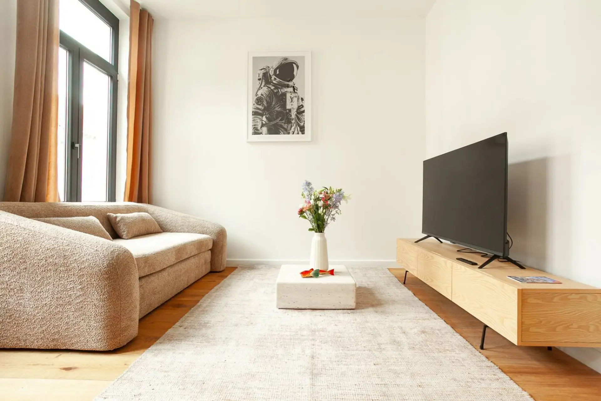 Bright living room w/ cozy sofa, wall-mounted TV & large windows letting in natural light