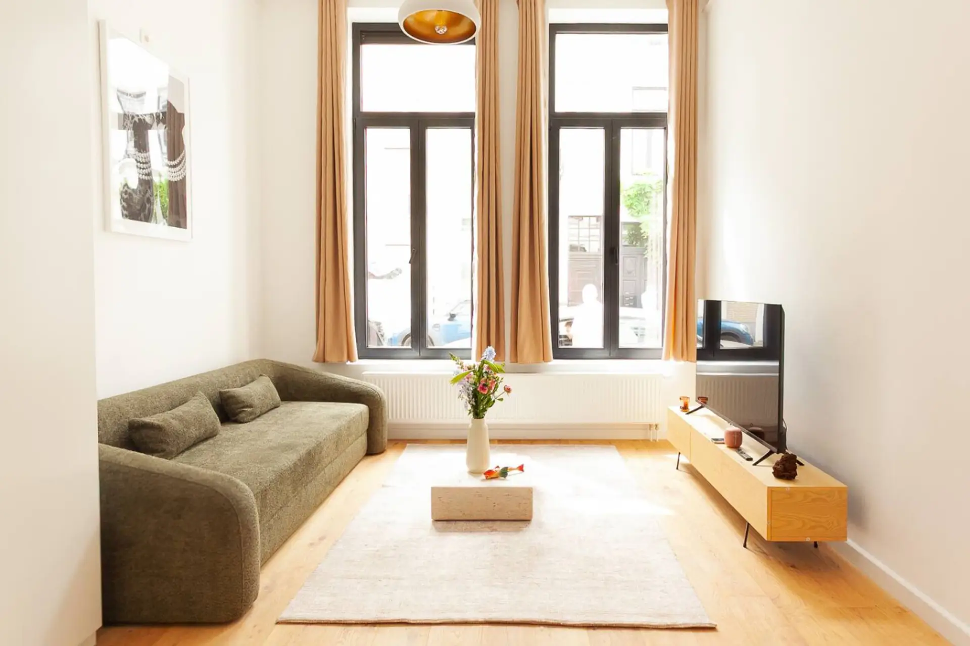 Bright living area w/ cozy sofa, TV & tall windows letting in soft natural light