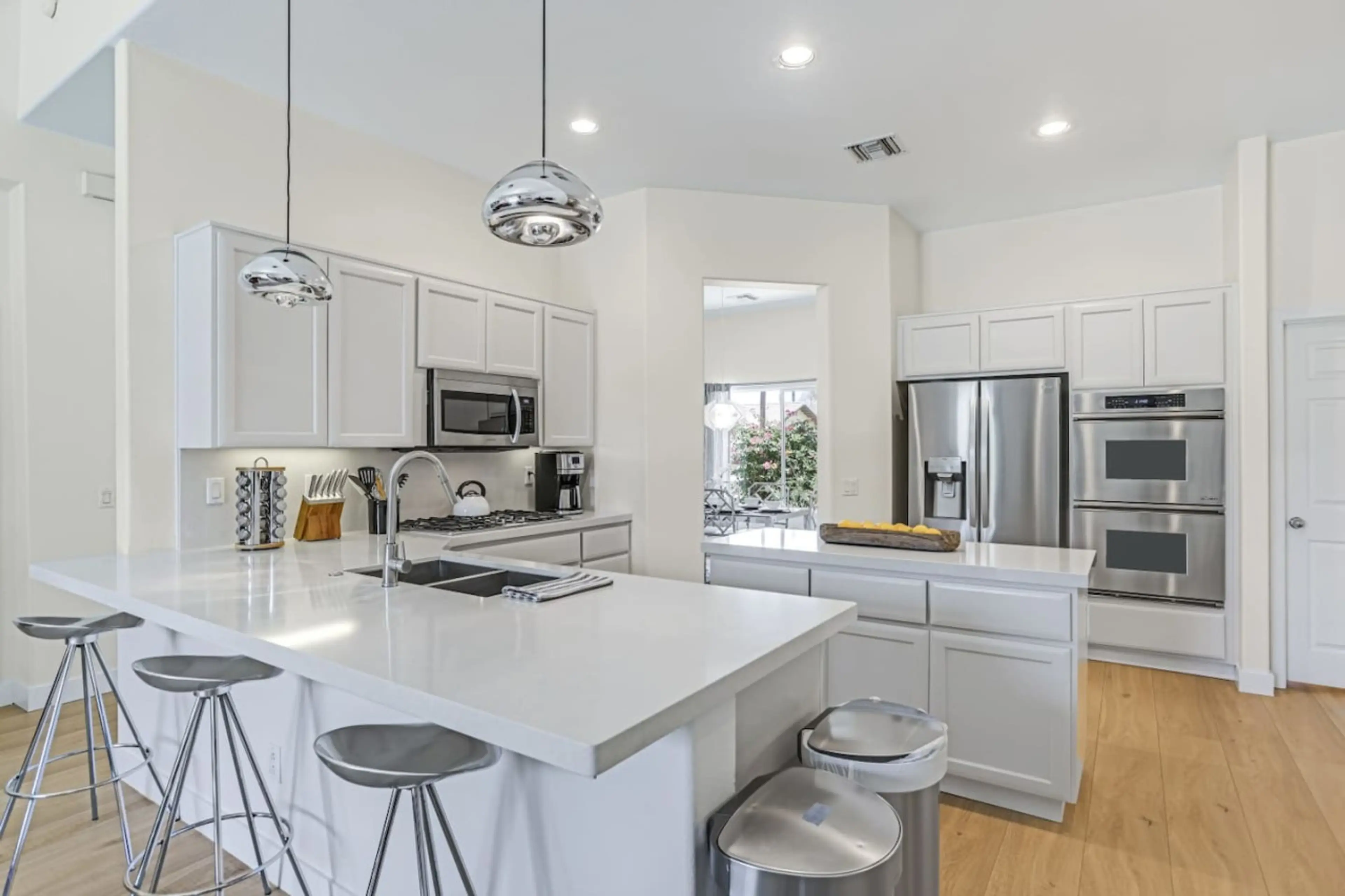 Modern fully equipped kitchen, featuring sleek white cabinetry, warm wood flooring, and high-end stainless steel appliances, offers a stylish and inviting space for cooking and gathering.