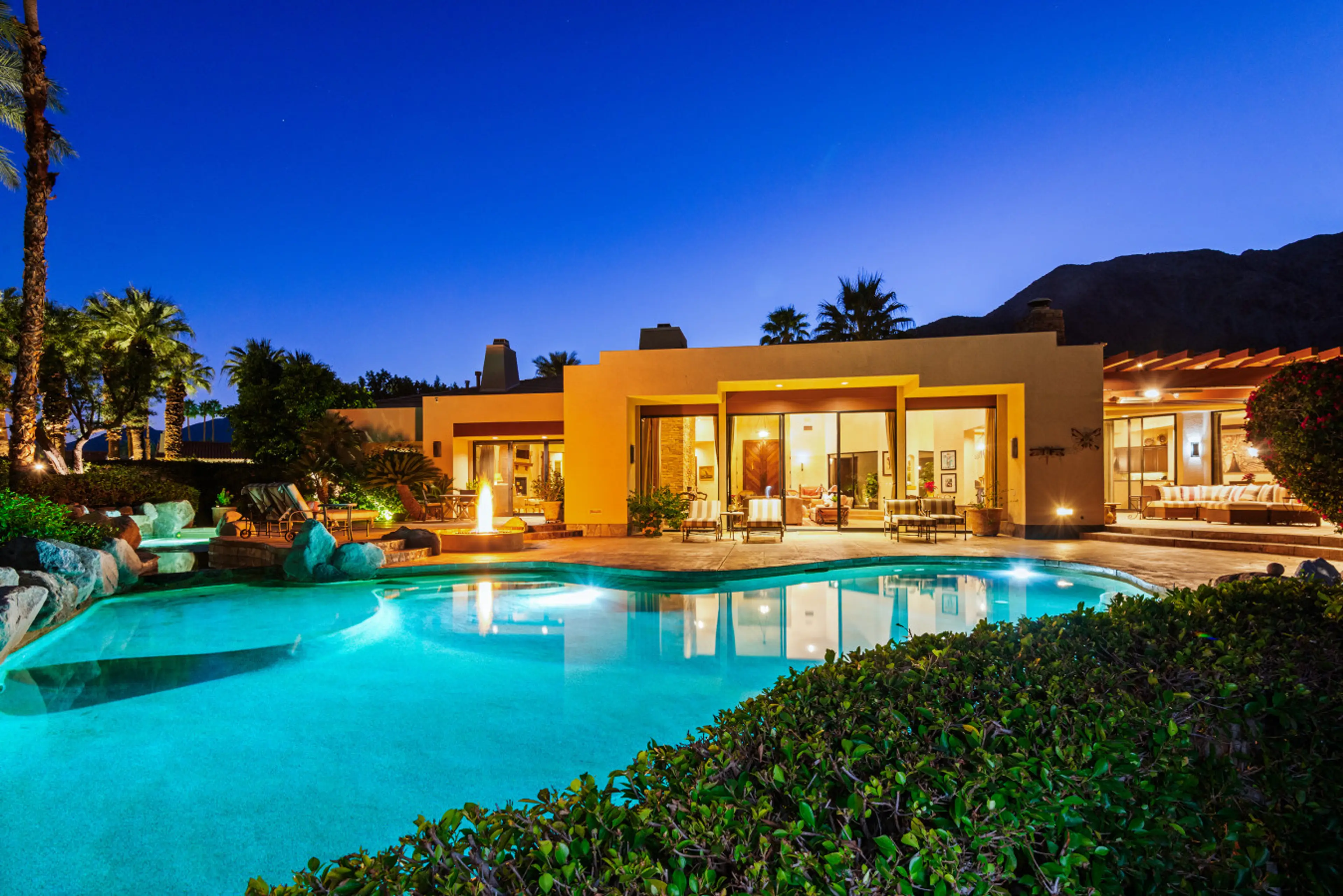 As the sun sets, the villa comes alive—glowing interiors, a shimmering pool, and mountain silhouettes create the perfect desert evening retreat.