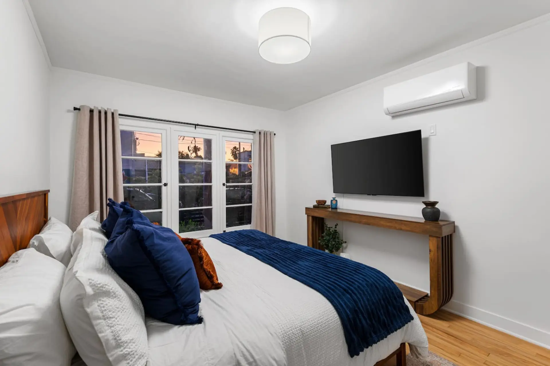 Serene king bedroom featuring fresh white luxury bedding, privacy curtains, entertainment-ready TV, and air conditioning/heat.