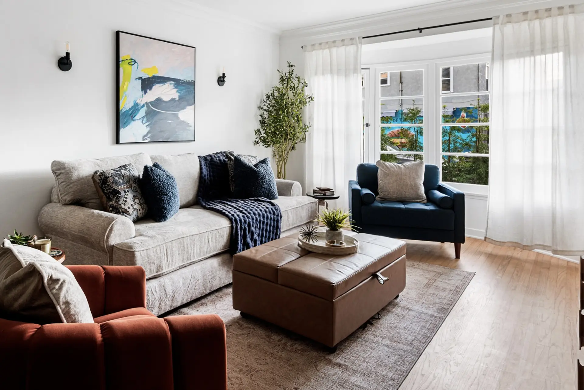 Airy living space featuring a plush sofa, expansive bay window to enjoy the Pacific breeze, and flowing white curtains.