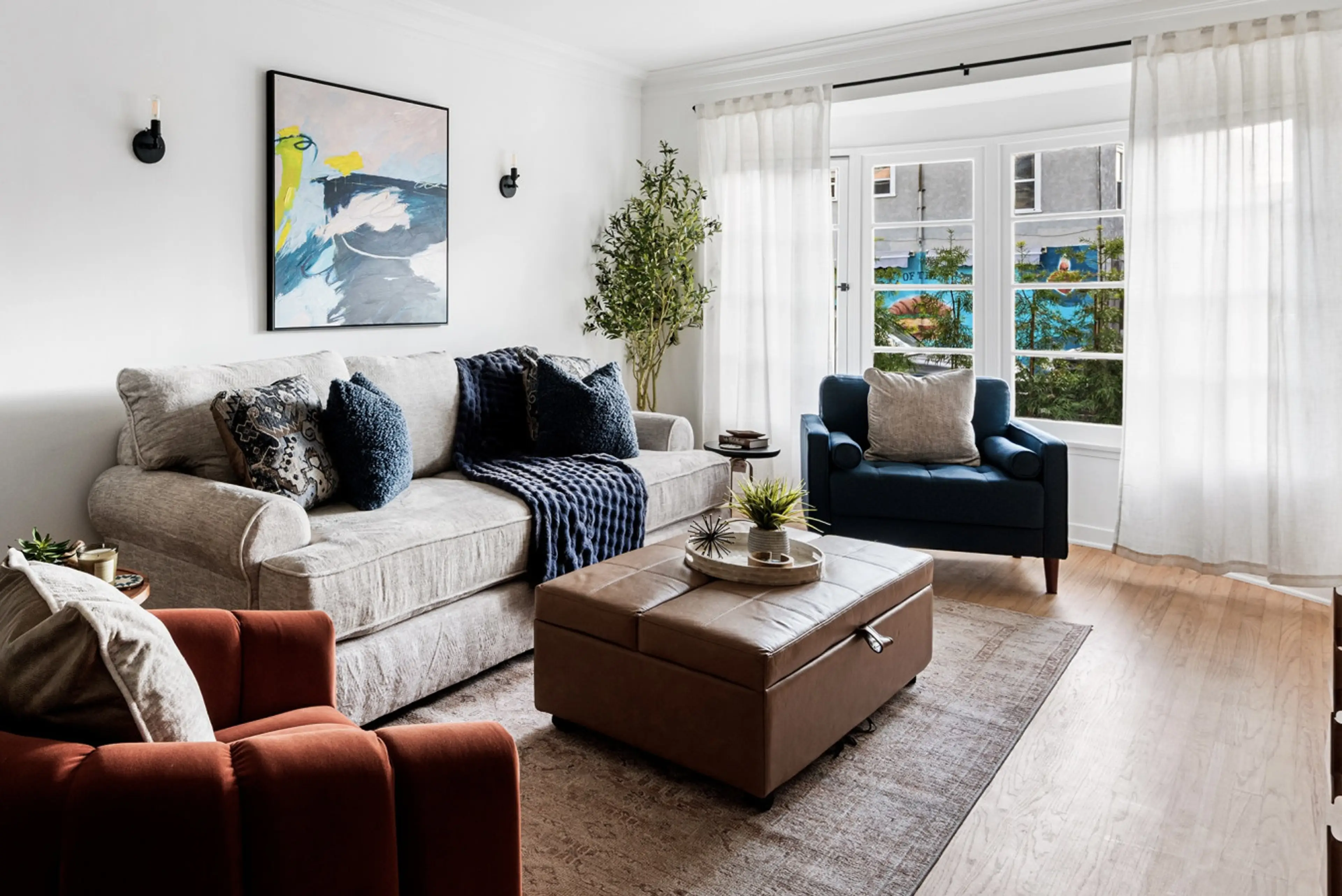 Airy living space featuring a plush sofa, expansive bay window to enjoy the Pacific breeze, and flowing white curtains.