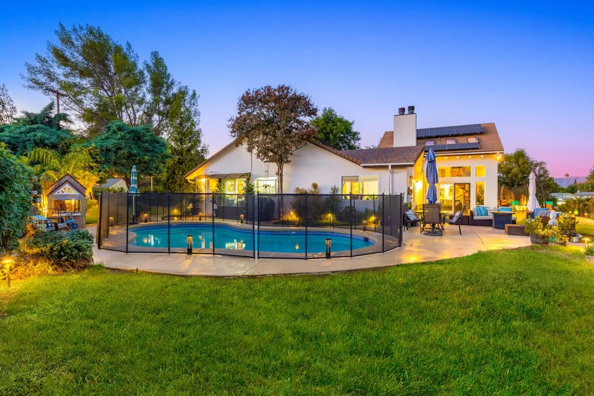 A fully renovated West Hills home glowing at dusk — the private pool, lush lawn, and warm interior lighting all come together in one stunning first impression.