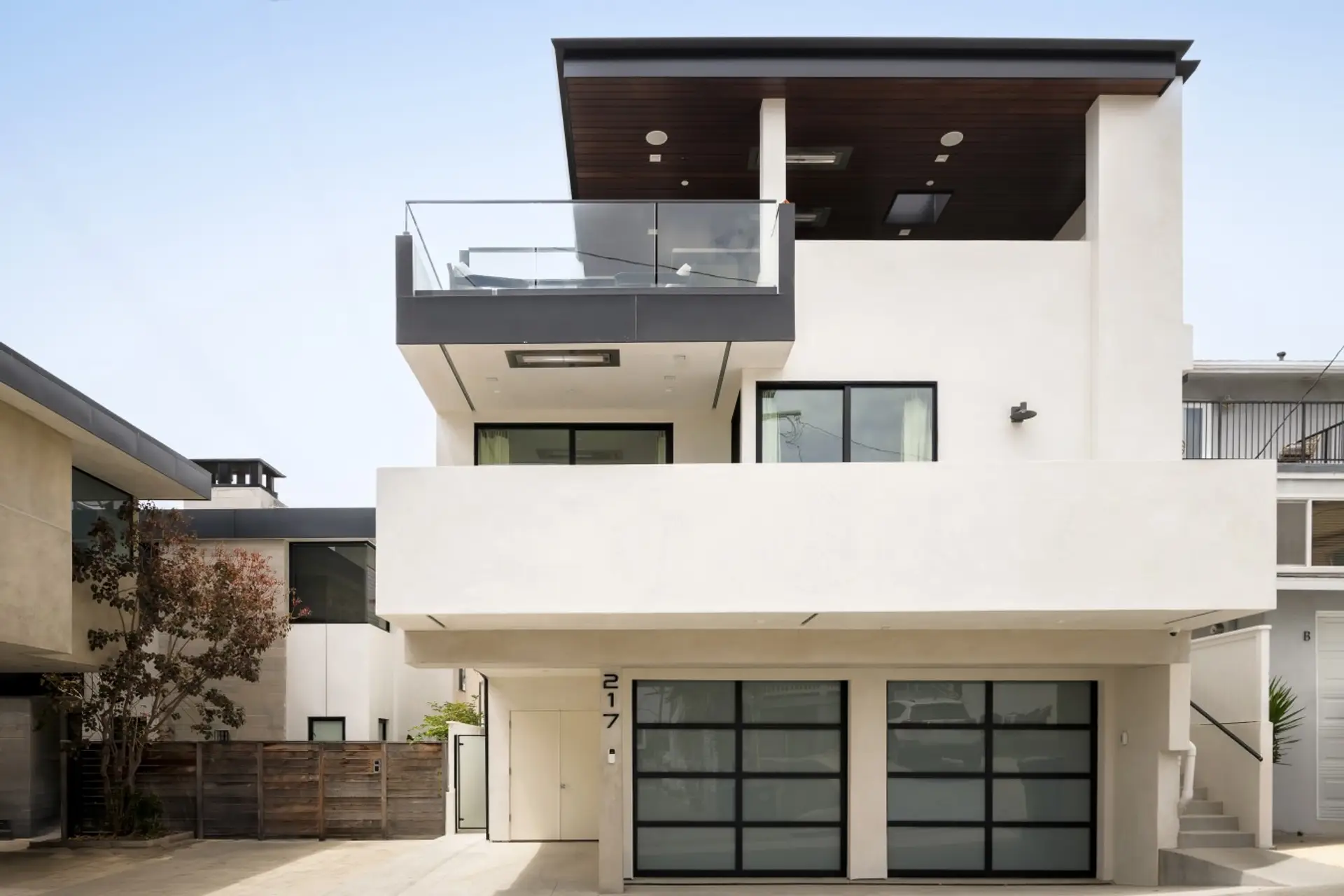 A striking contemporary façade with clean architectural lines, expansive windows, and a private balcony creates a sophisticated first impression, complemented by a covered outdoor terrace and sleek garage doors.