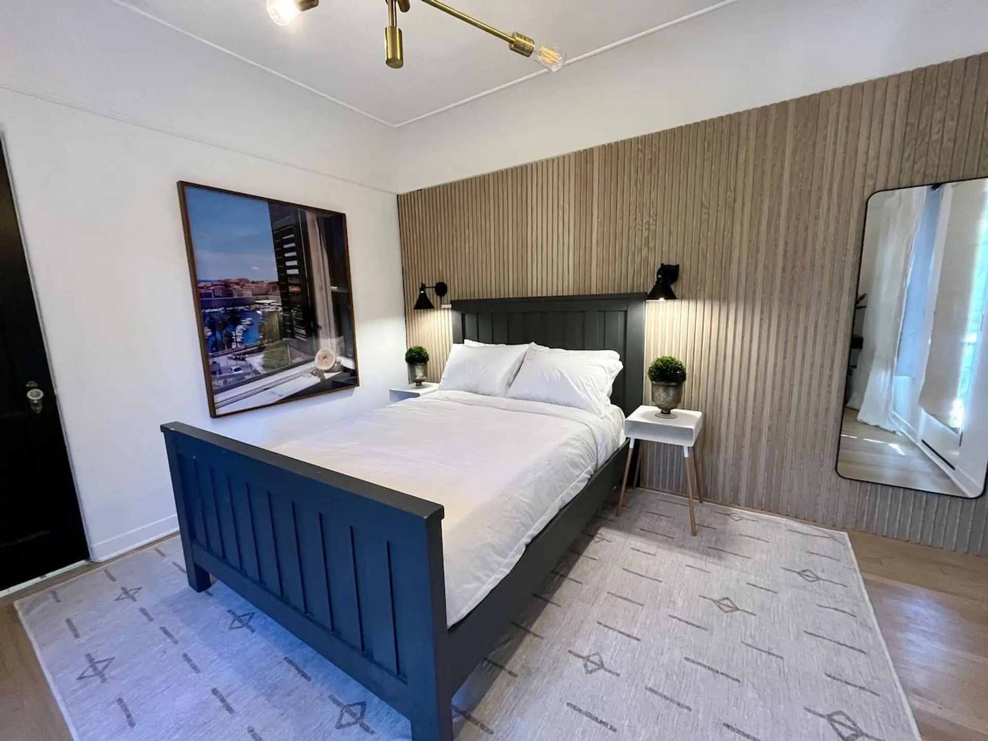 Cozy up in the plush full bed, framed by a warm wood-paneled accent wall and soft ambient lighting on both sides.