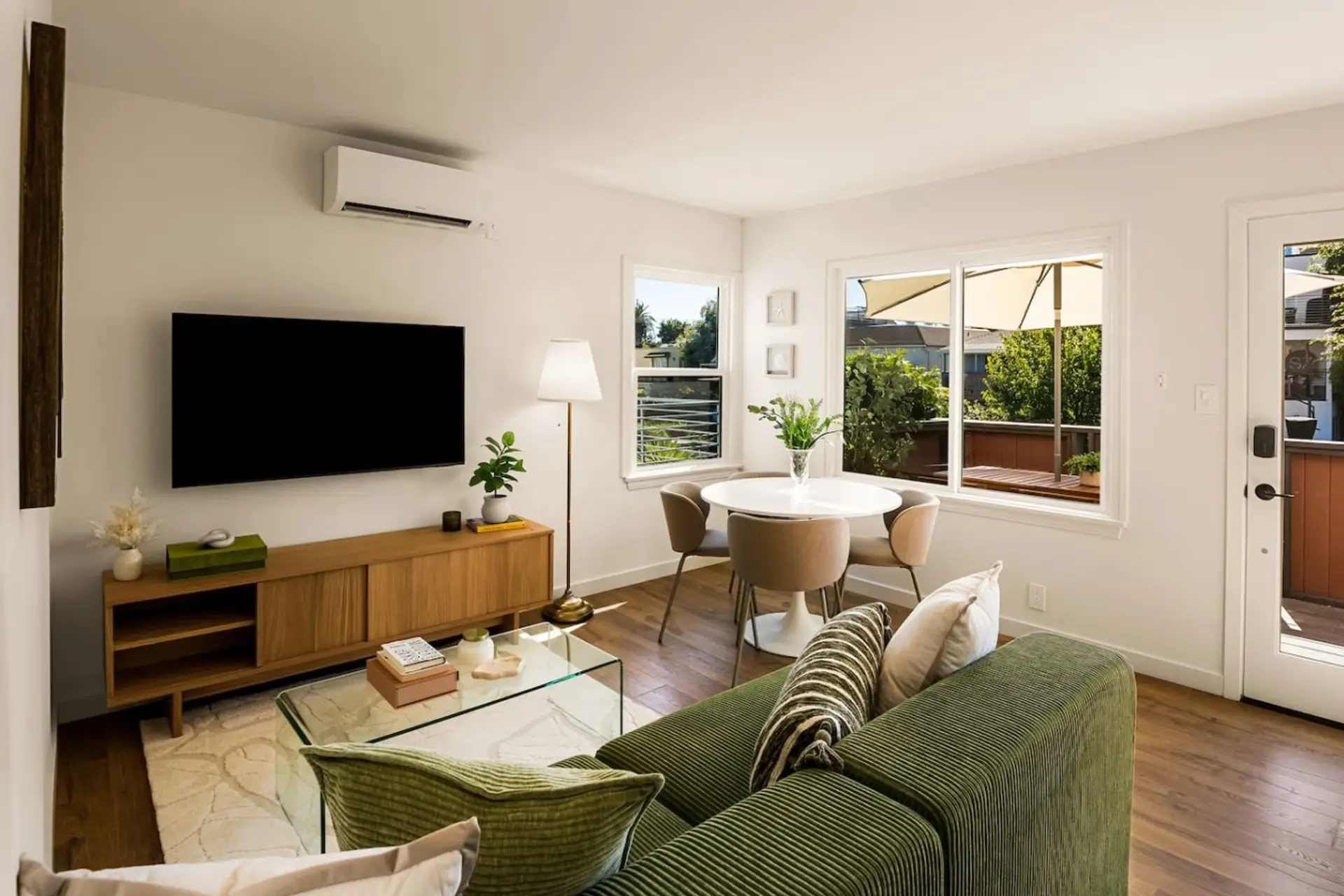 The living area opens up with wide plank hardwood floors, a plush green sofa, and natural light pouring in from the canal-facing windows.