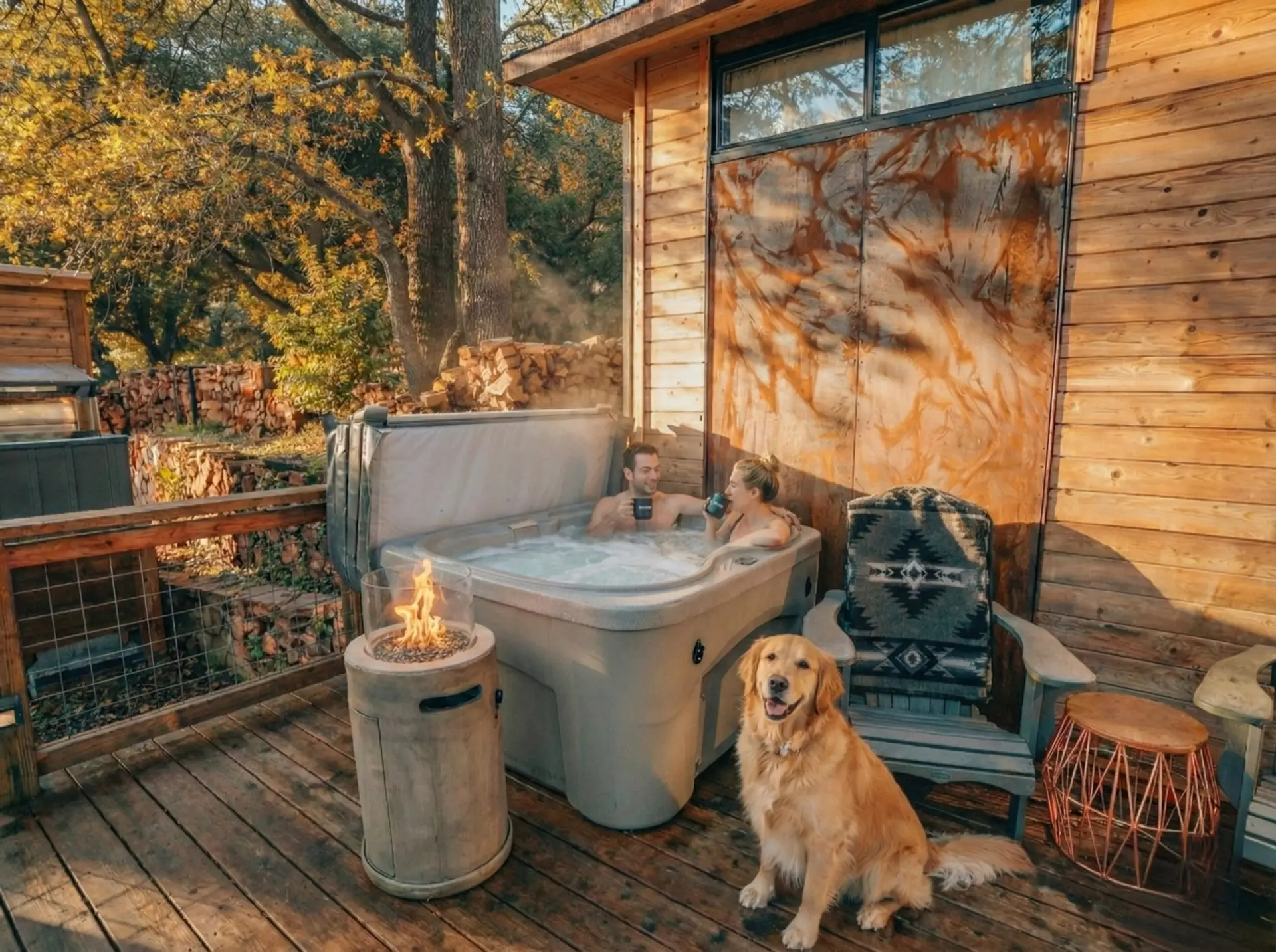 Pet-friendly hot tub soak surrounded by fall color and stacked firewood.