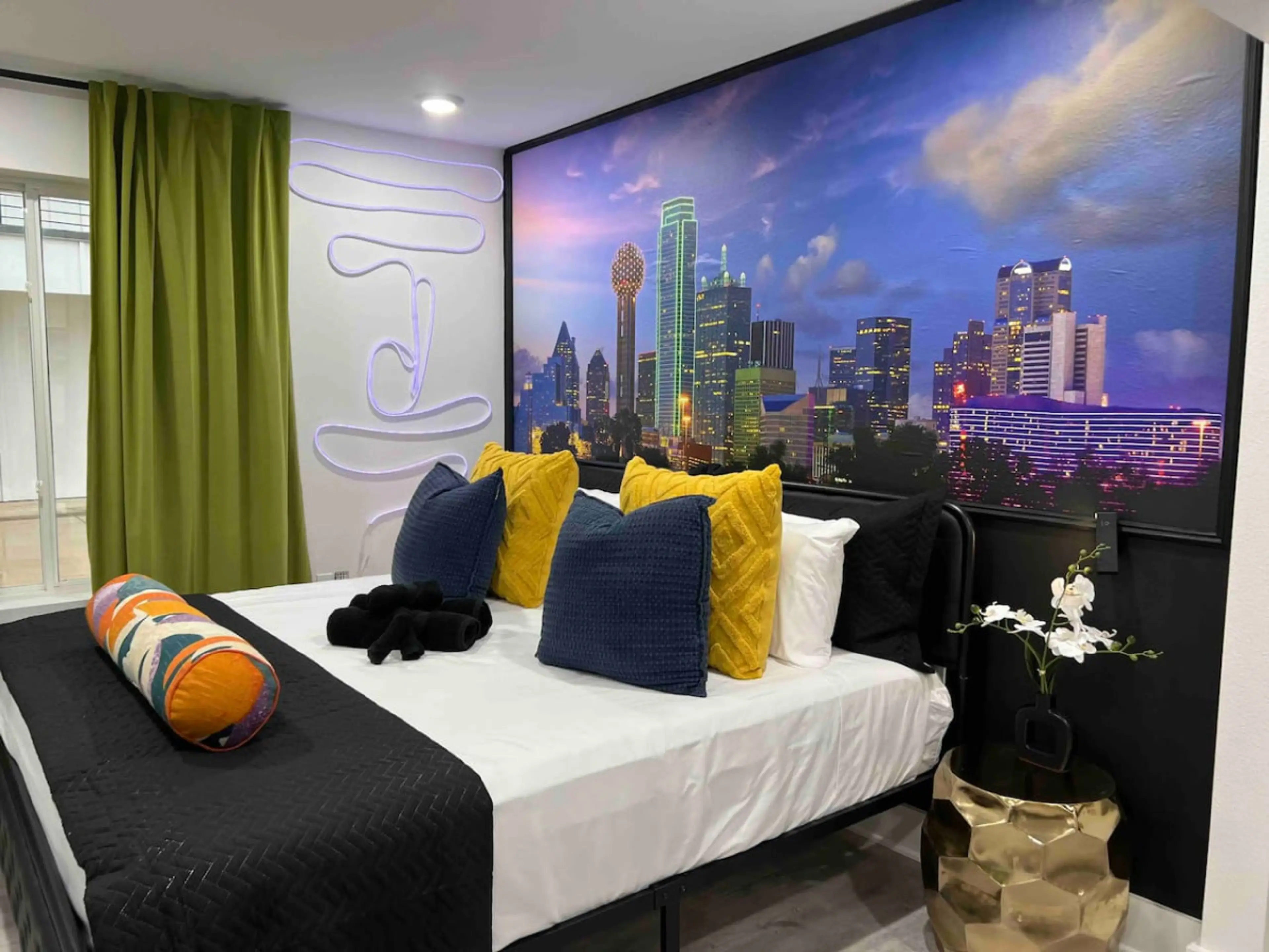 Stylish king bedroom featuring bold black, white and yellow tones, fresh green accents and a custom mural of the Dallas skyline for a one-of-a-kind stay.