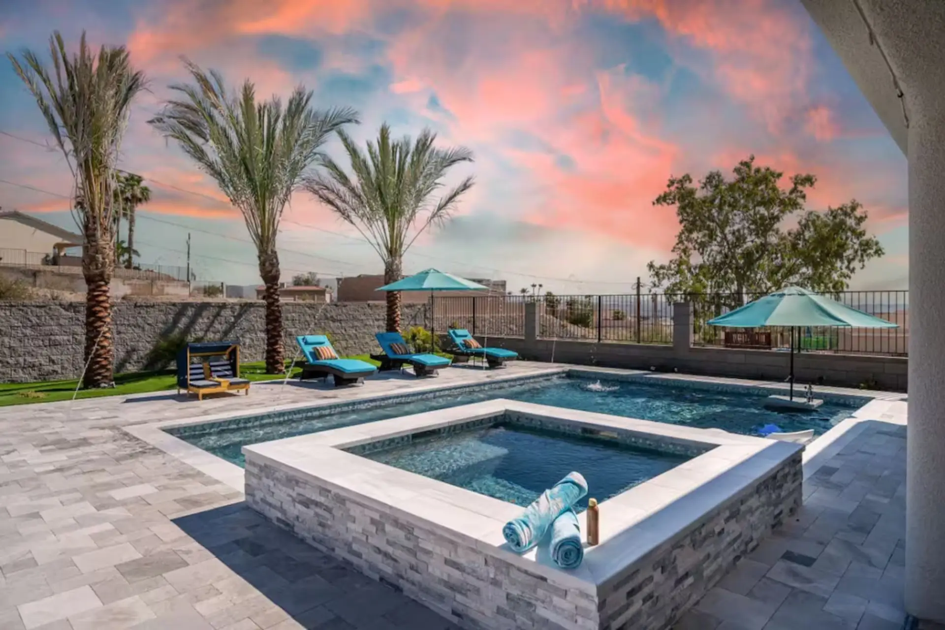Sunset pool + spa with stone-surround hot tub, lounge chairs, and palm trees — the shot guests screenshot before they book