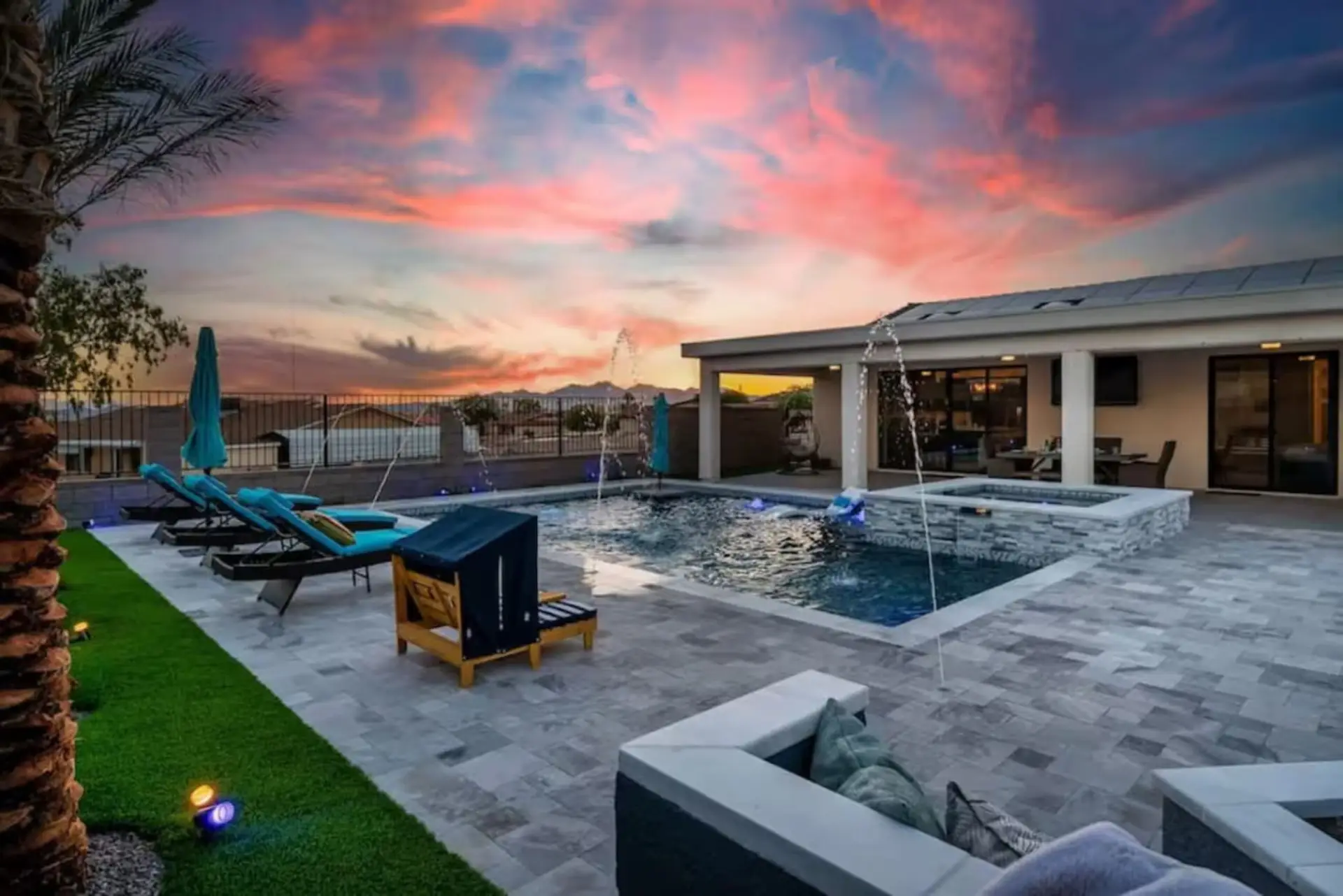 Sunset backyard with pool fountains, spa, chaise loungers on turf lawn, and mountain backdrop — that sky alone will close the booking