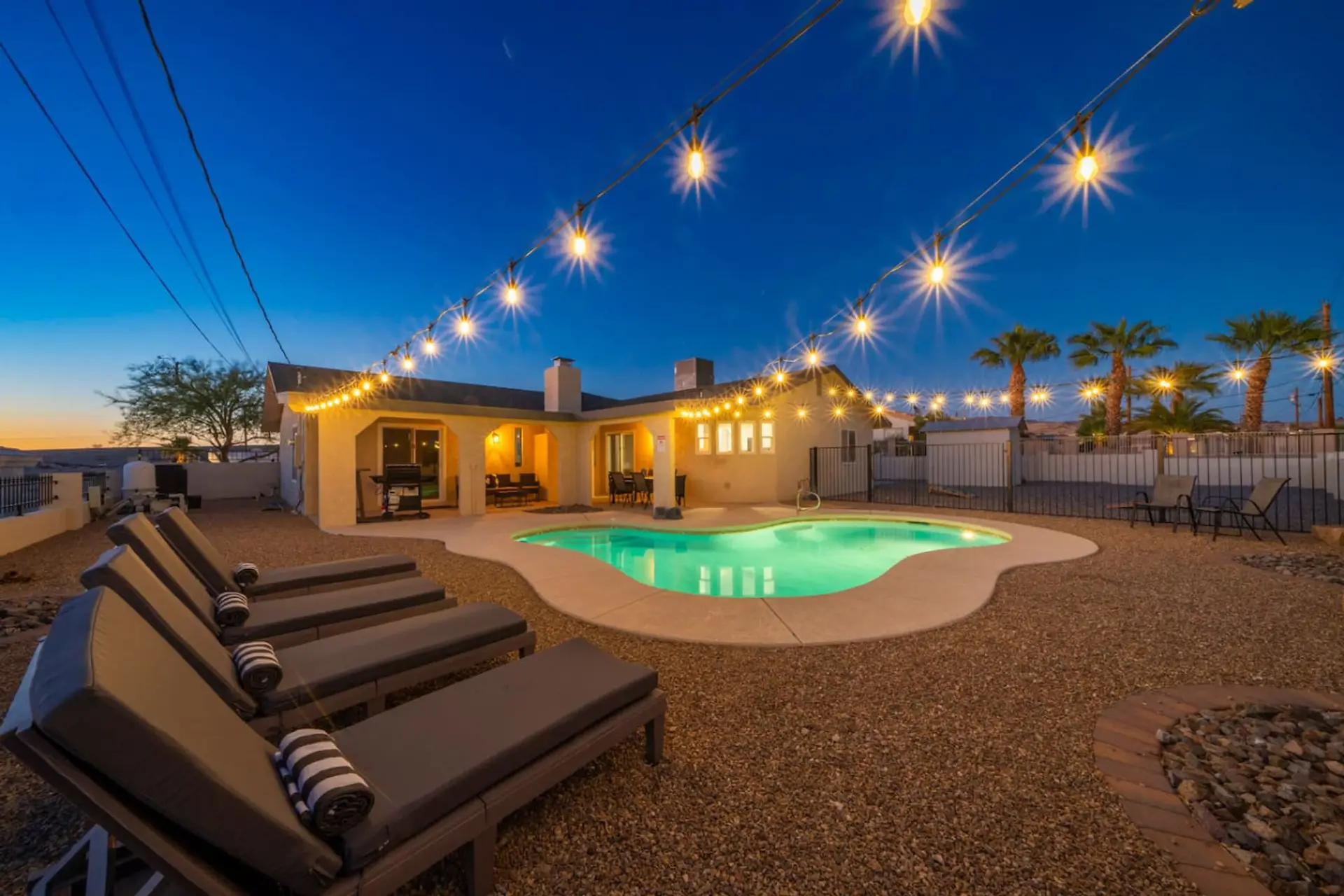 Twilight backyard — lit pool, string lights overhead, and loungers ready. The shot guests screenshot before they book.