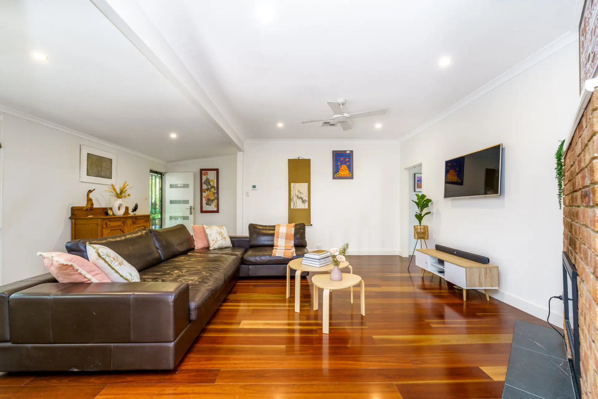 A cosy living room with a leather lounge, smart TV, and electric fireplace sets the perfect ambiance. Modern artwork and large windows let you enjoy the surrounding greenery while relaxing in style.
