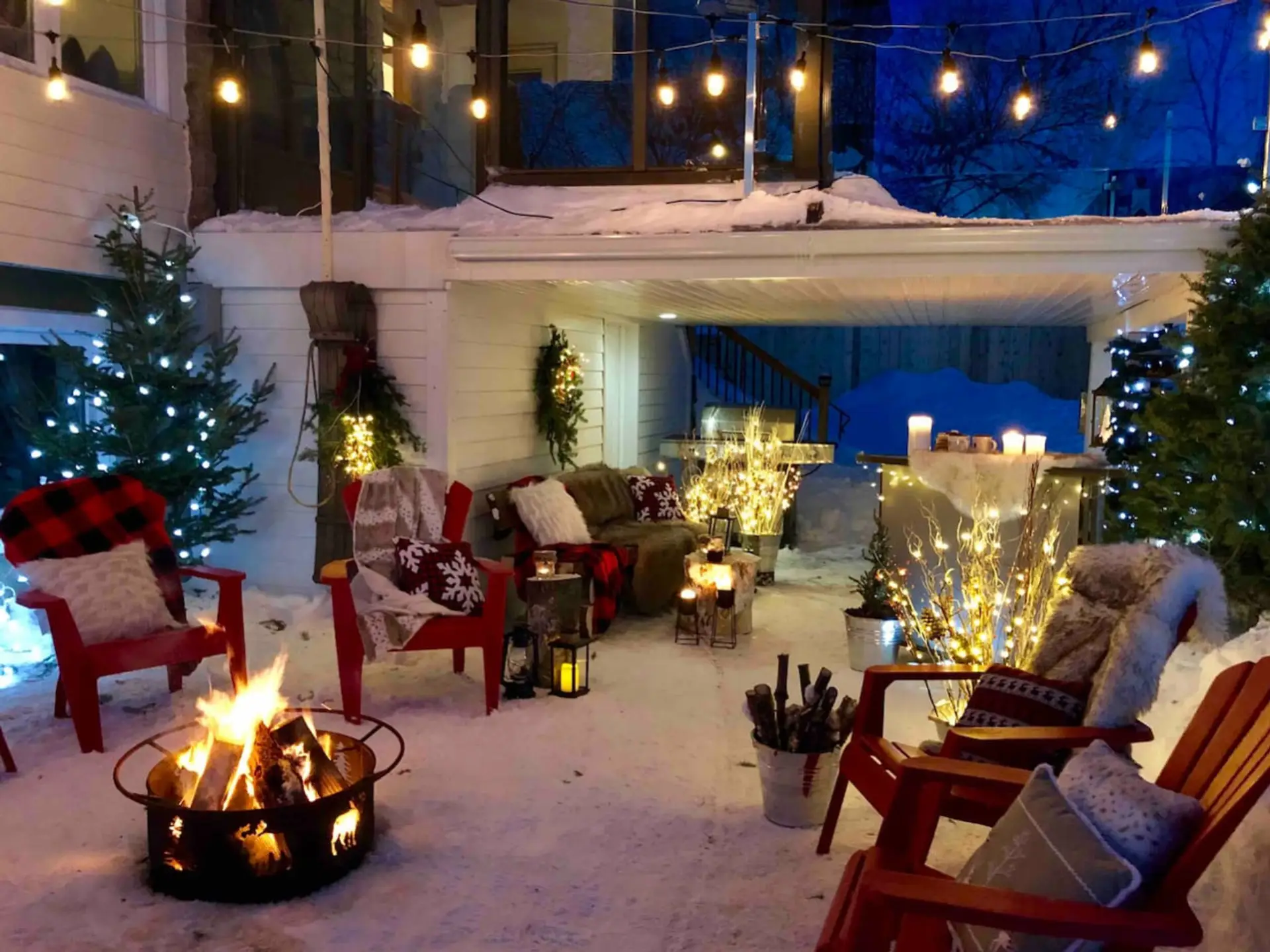 A cozy winter outdoor lounge with fire pit and festive lighting