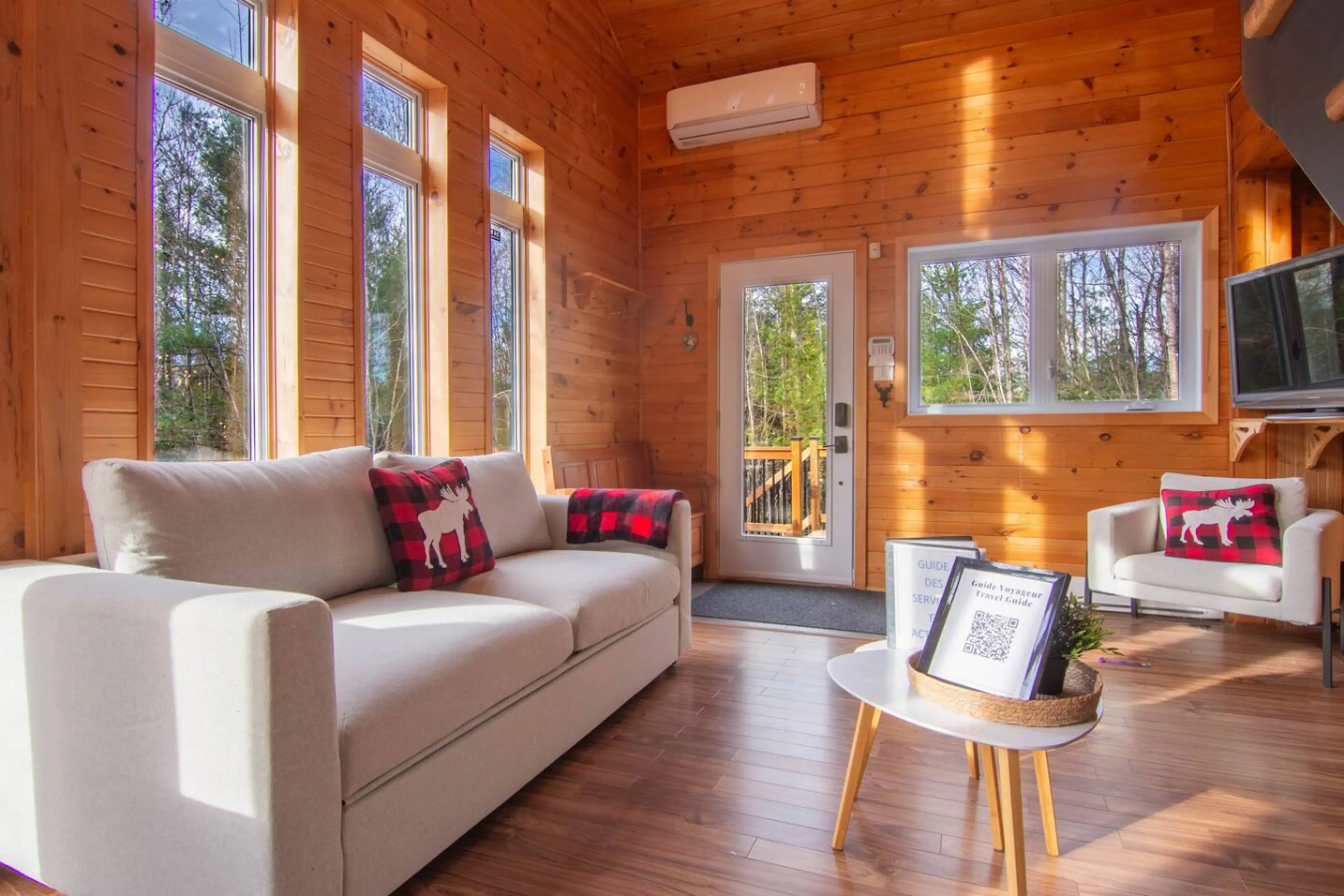 A living room bathed in light thanks to its tall windows and cathedral ceiling. The perfect place to relax, read a book or enjoy a coffee overlooking nature.