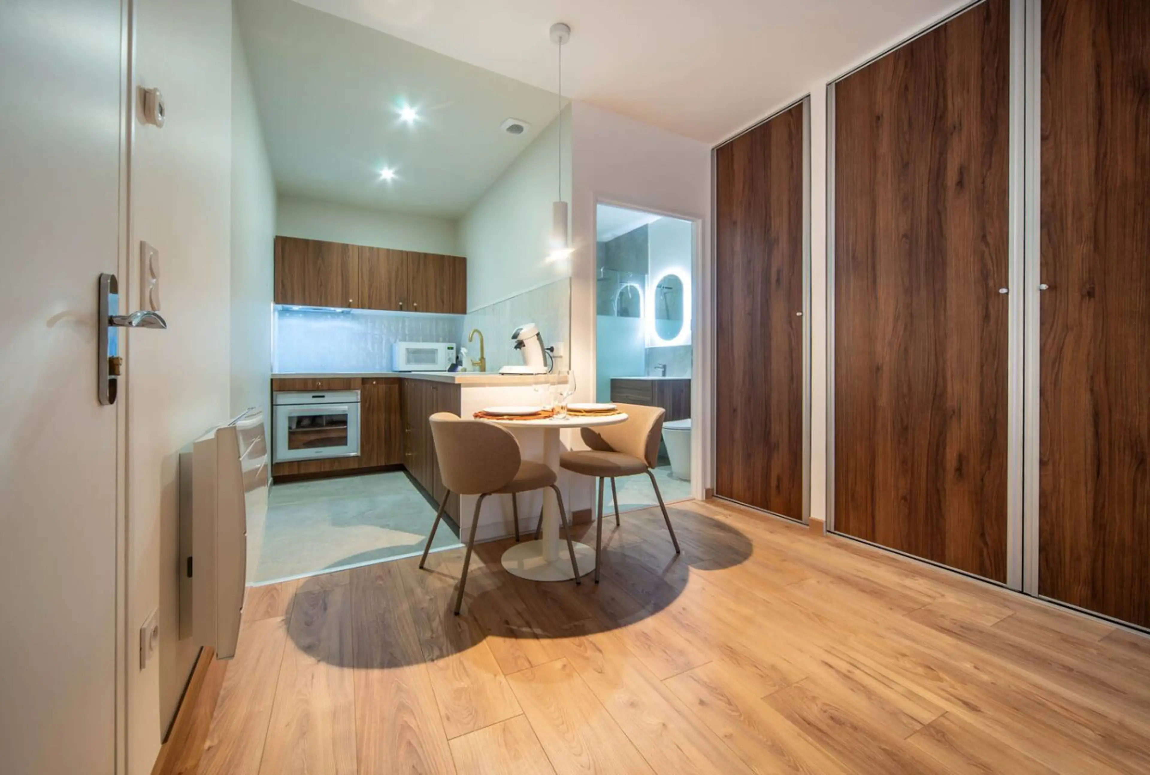 Séjour lumineux avec cuisine ouverte, table ronde, armoires en bois et sol en parquet chaleureux