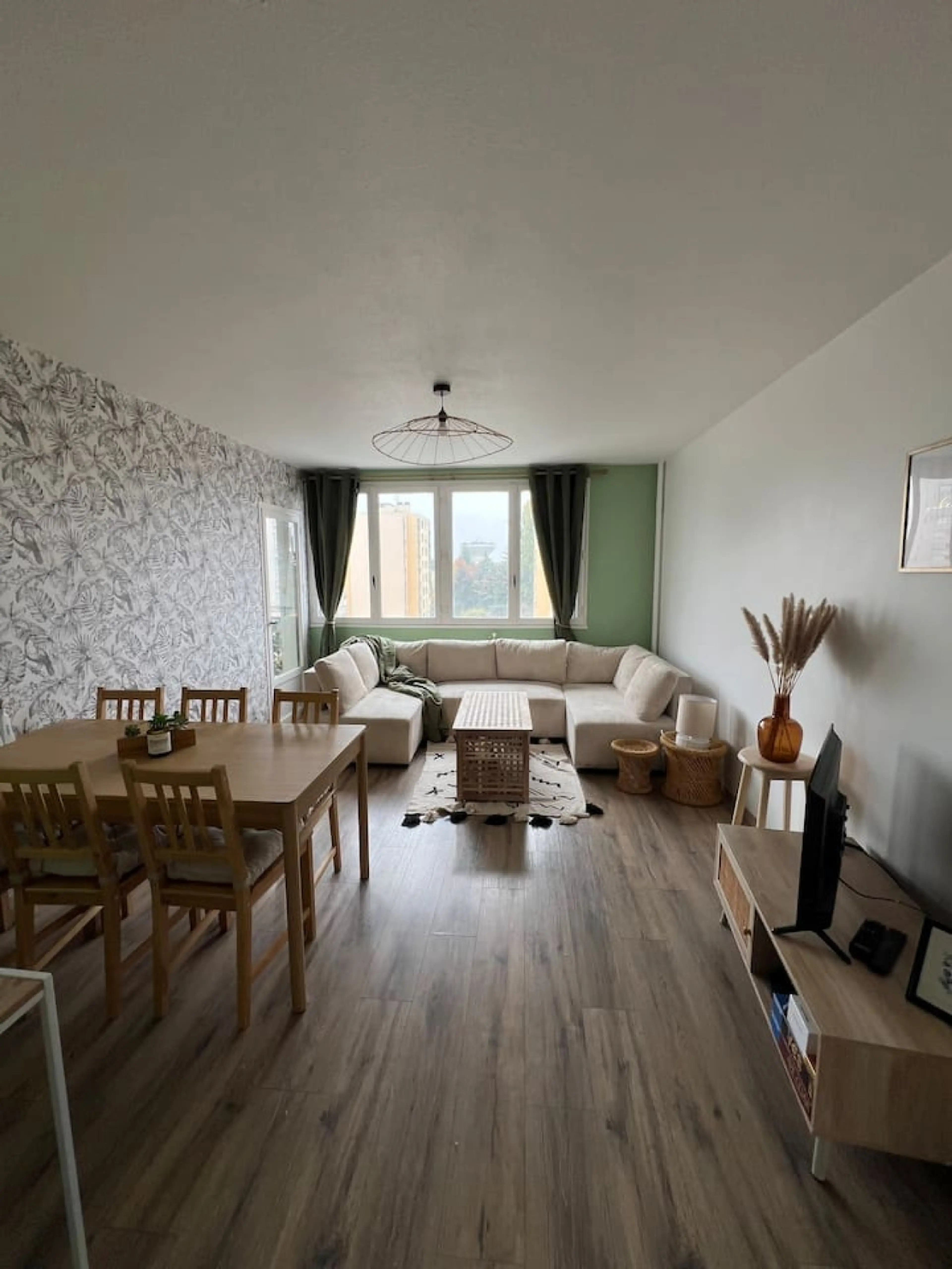 Spacieux séjour lumineux avec canapé confortable, salle à manger bois, papier peint tendance et grandes fenêtres