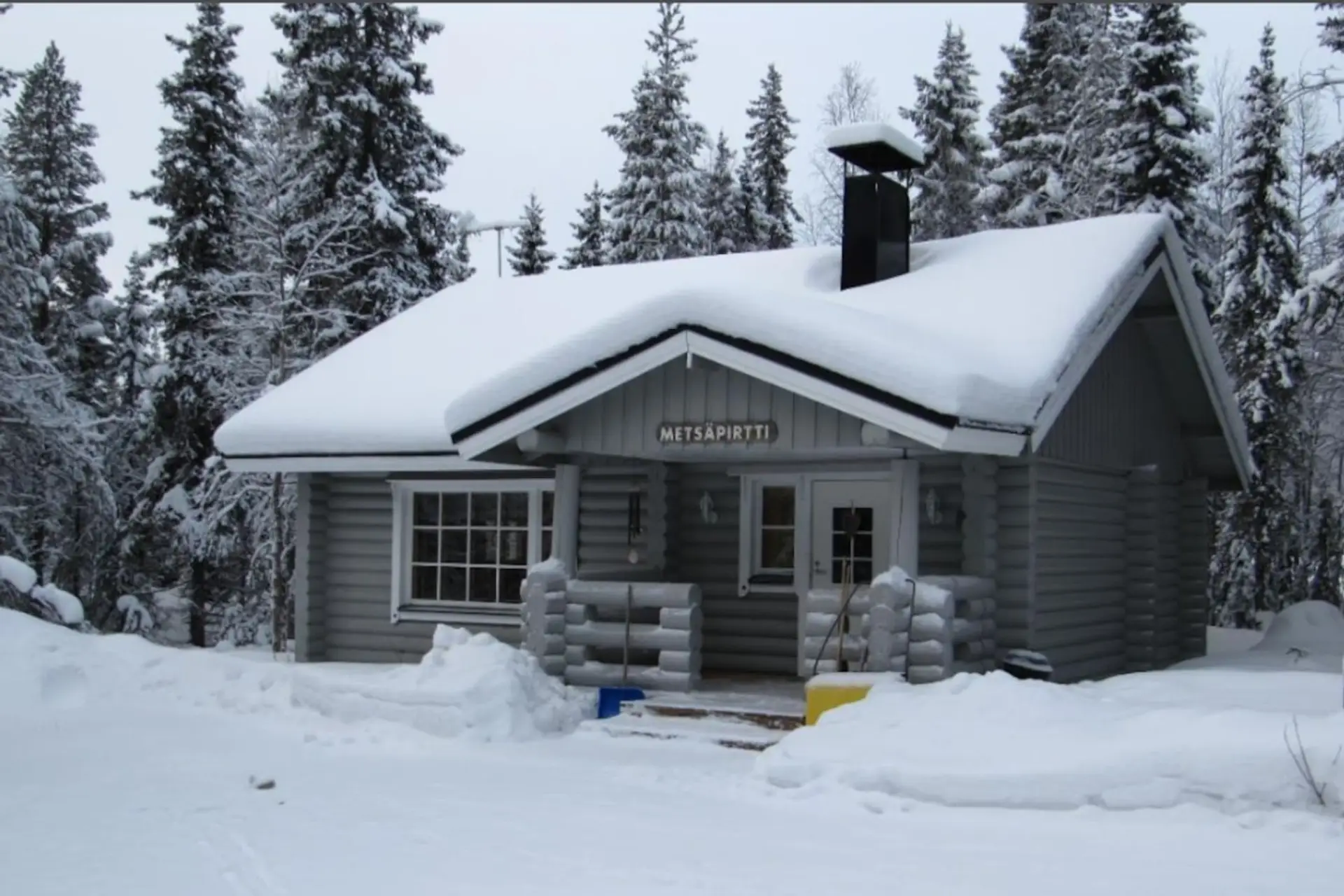 Traditional log cabin surrounded by snow-covered pine forest.