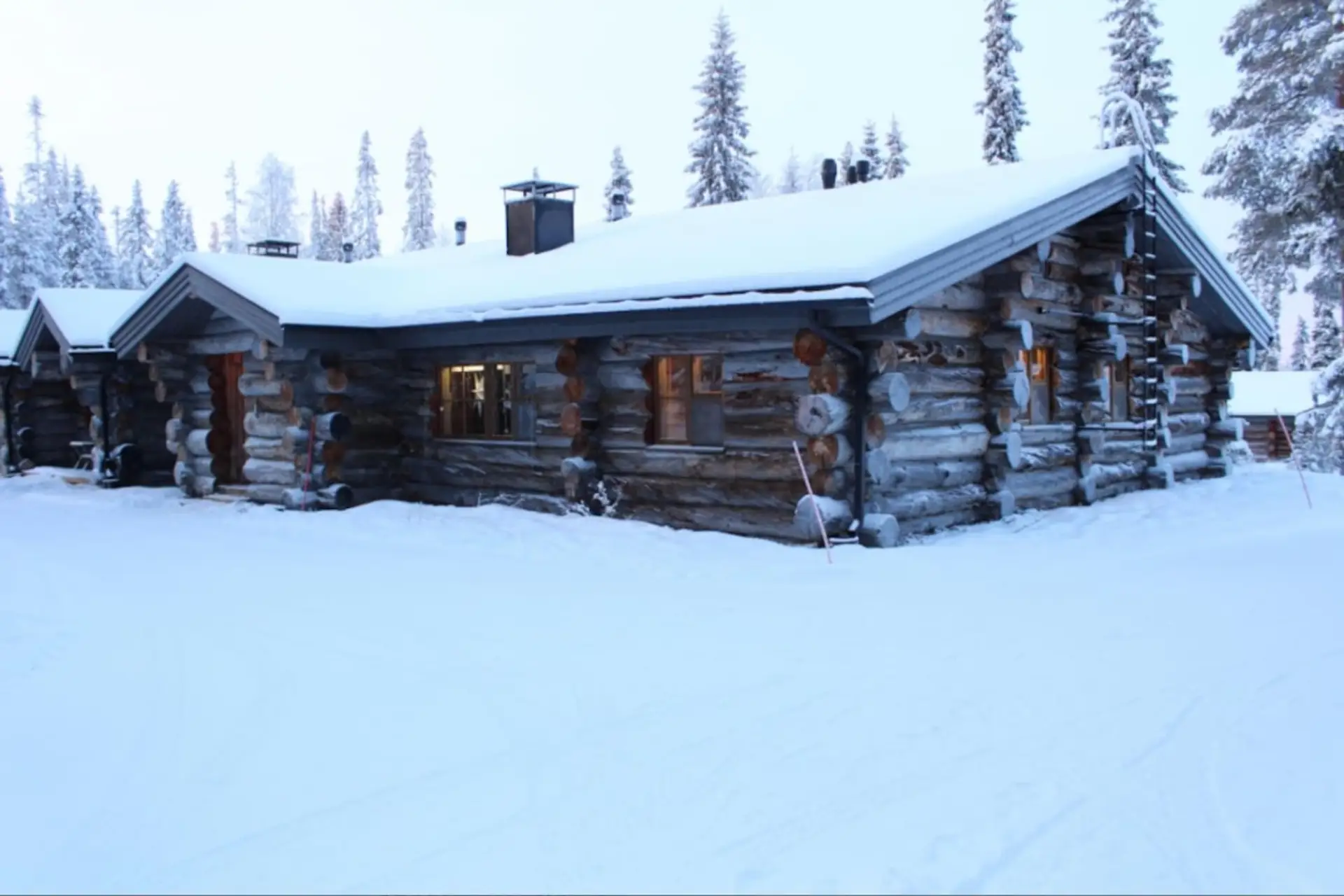 The kelo-log chalet surrounded by deep snow on a winter evening.
