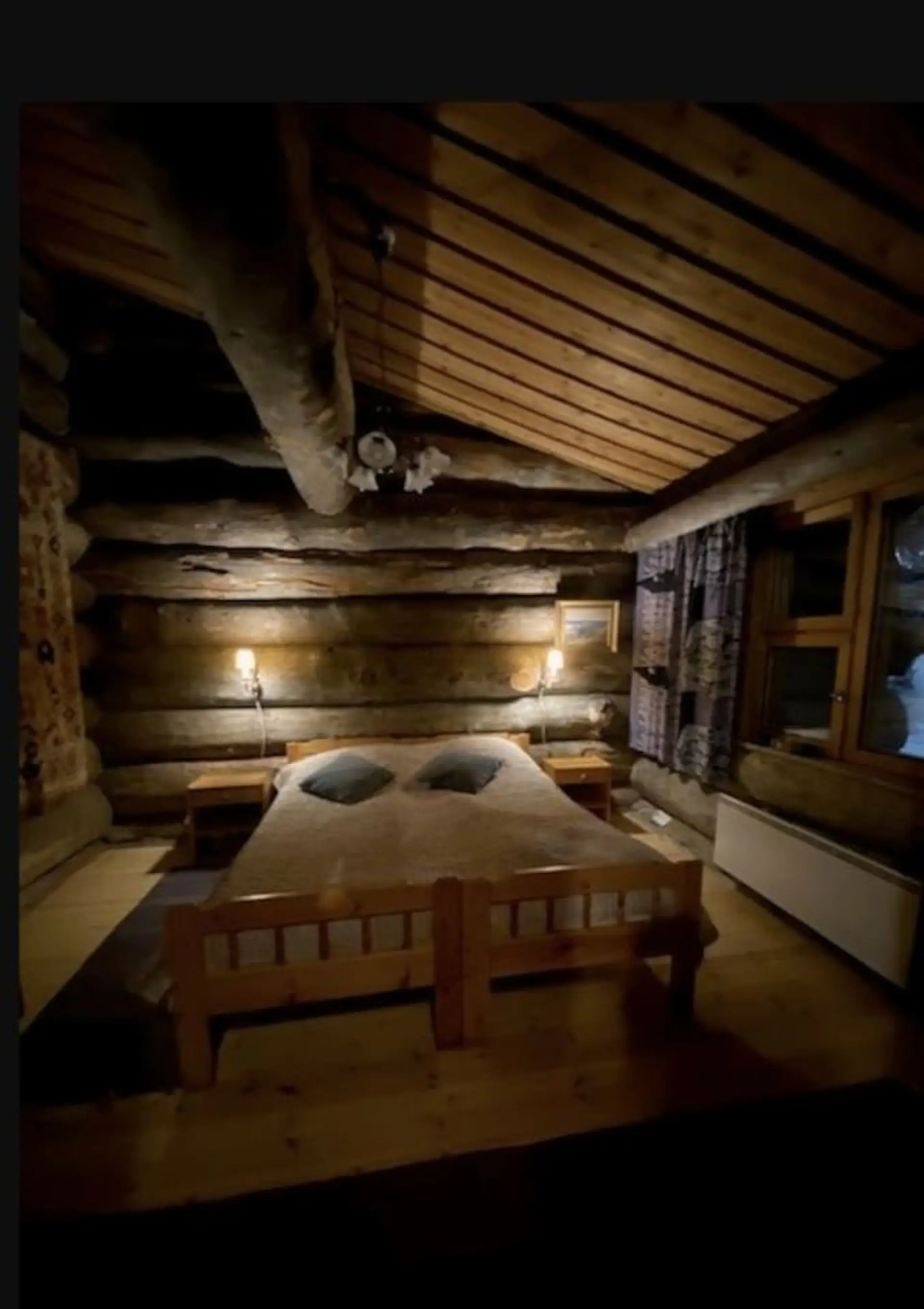 Double bed in the log-walled bedroom with a window and wall lamps.