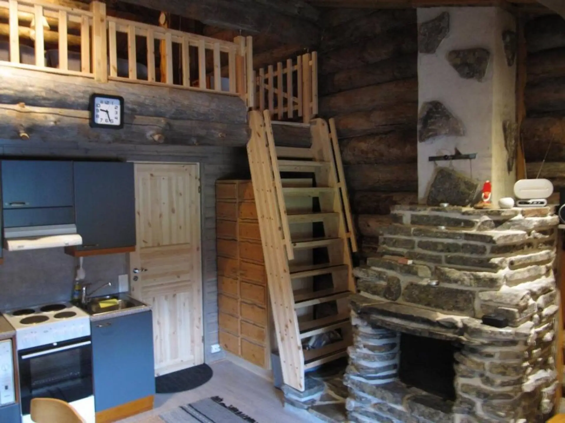 Open-plan interior showing the kitchen, the stairs up to the loft, and the stone fireplace.