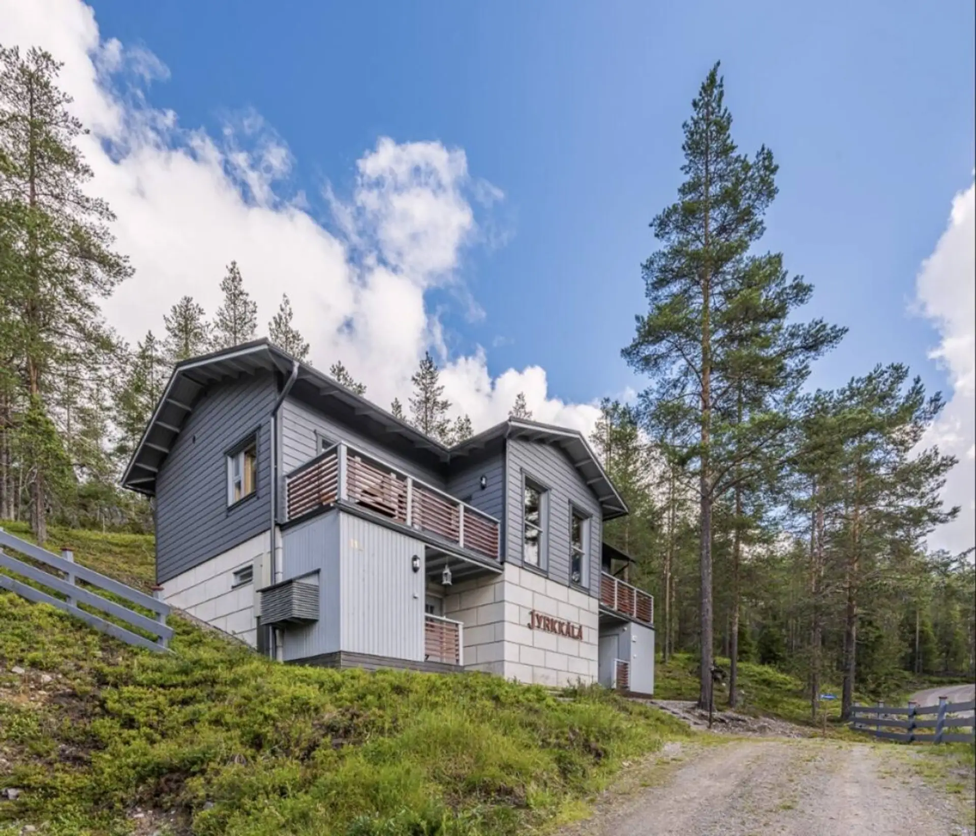 Exterior view of the wooden two-storey semi-detached house surrounded by pine forest.