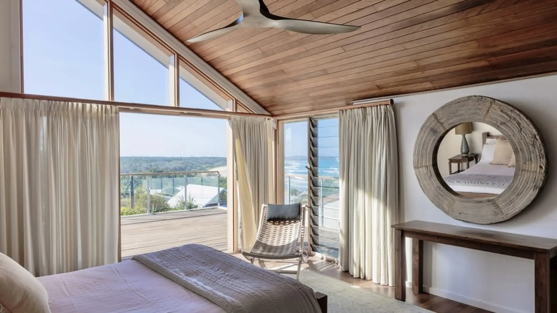 Master bedroom with ocean glimpses and a designer round mirror — light, airy and beachside.