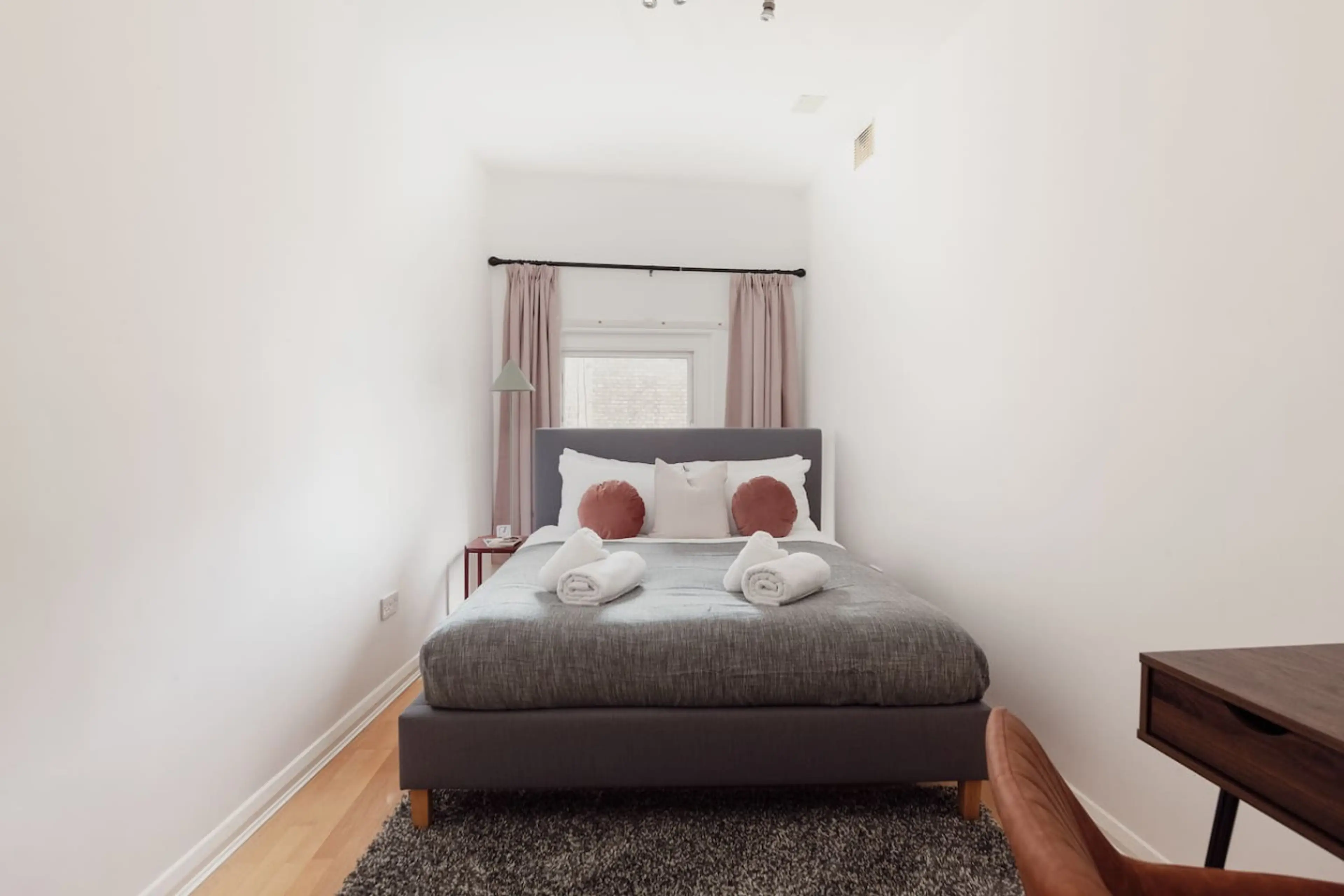 The centerpiece is a stylish gray upholstered bed with a tall headboard, dressed in soft gray bedding and complemented by white and rust-colored accent pillows.