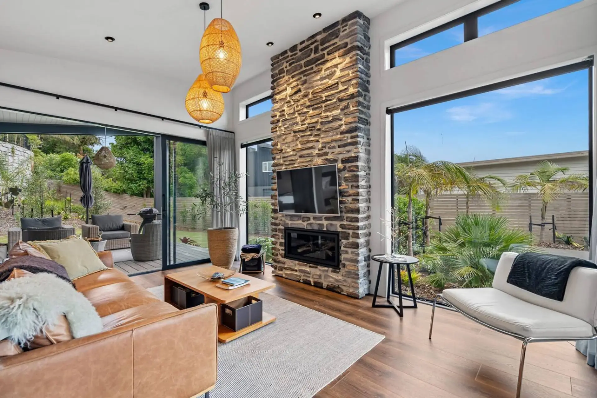 The lounge features a striking gas fireplace, TV screen with Chromecast, and timber floors, with oversized windows framing the lush subtropical garden. A comfortable, light-filled space to relax year-round, with seamless access to the outdoor areas.