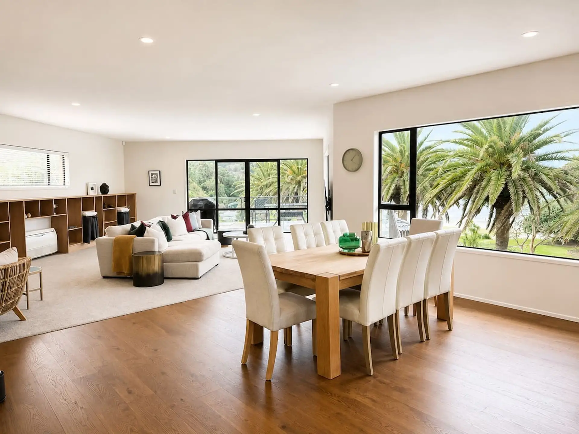 Bright open-plan living and dining on the upper level, framed by windows full of palms — gather everyone for meals and games, with extra perch at the breakfast bar seating four beside the table.