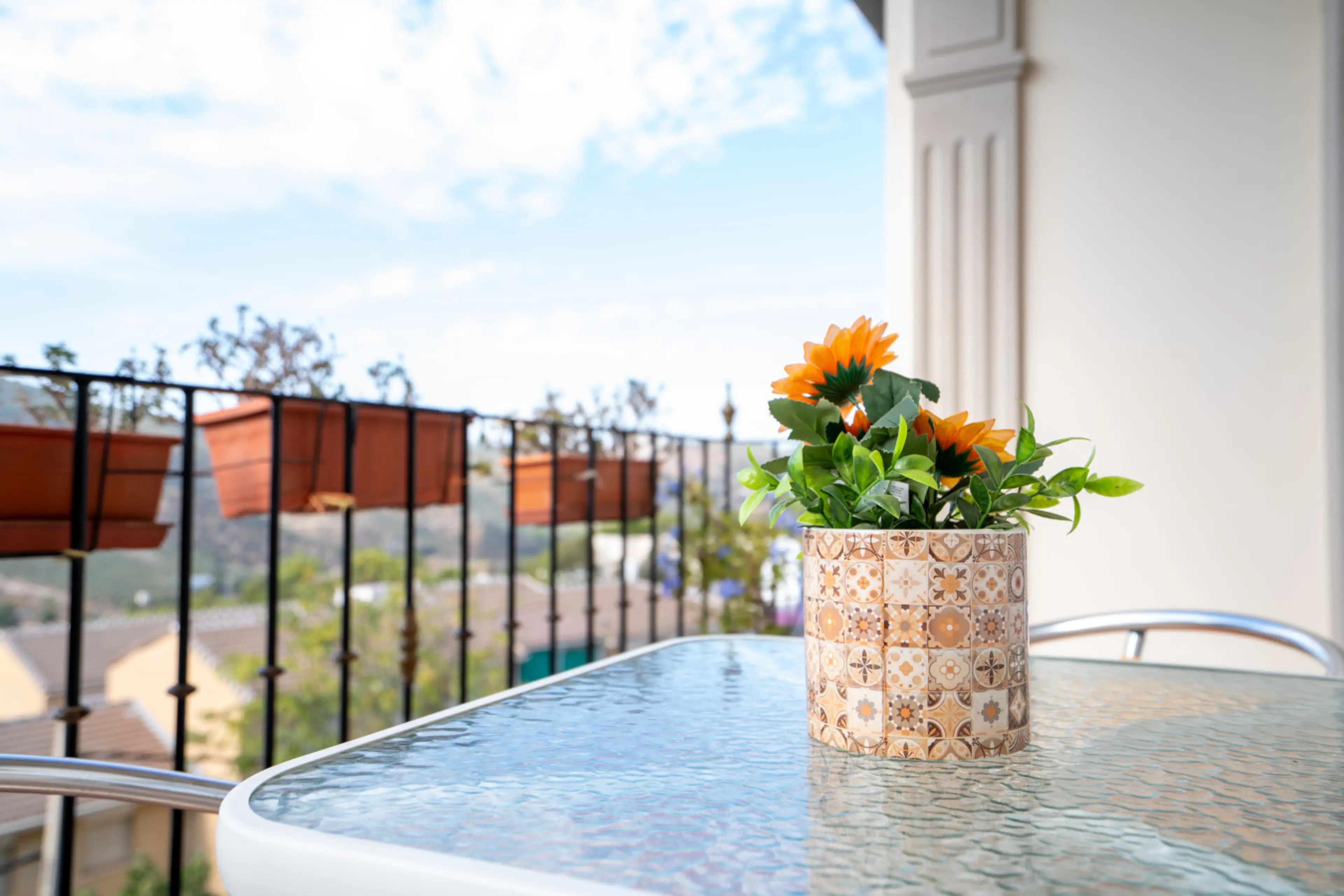 Pequeña terraza con mesa decorada y vistas despejadas. Un espacio encantador para disfrutar del desayuno o un café al aire libre. La combinación de flores y cerámica aporta un toque acogedor y mediterráneo.