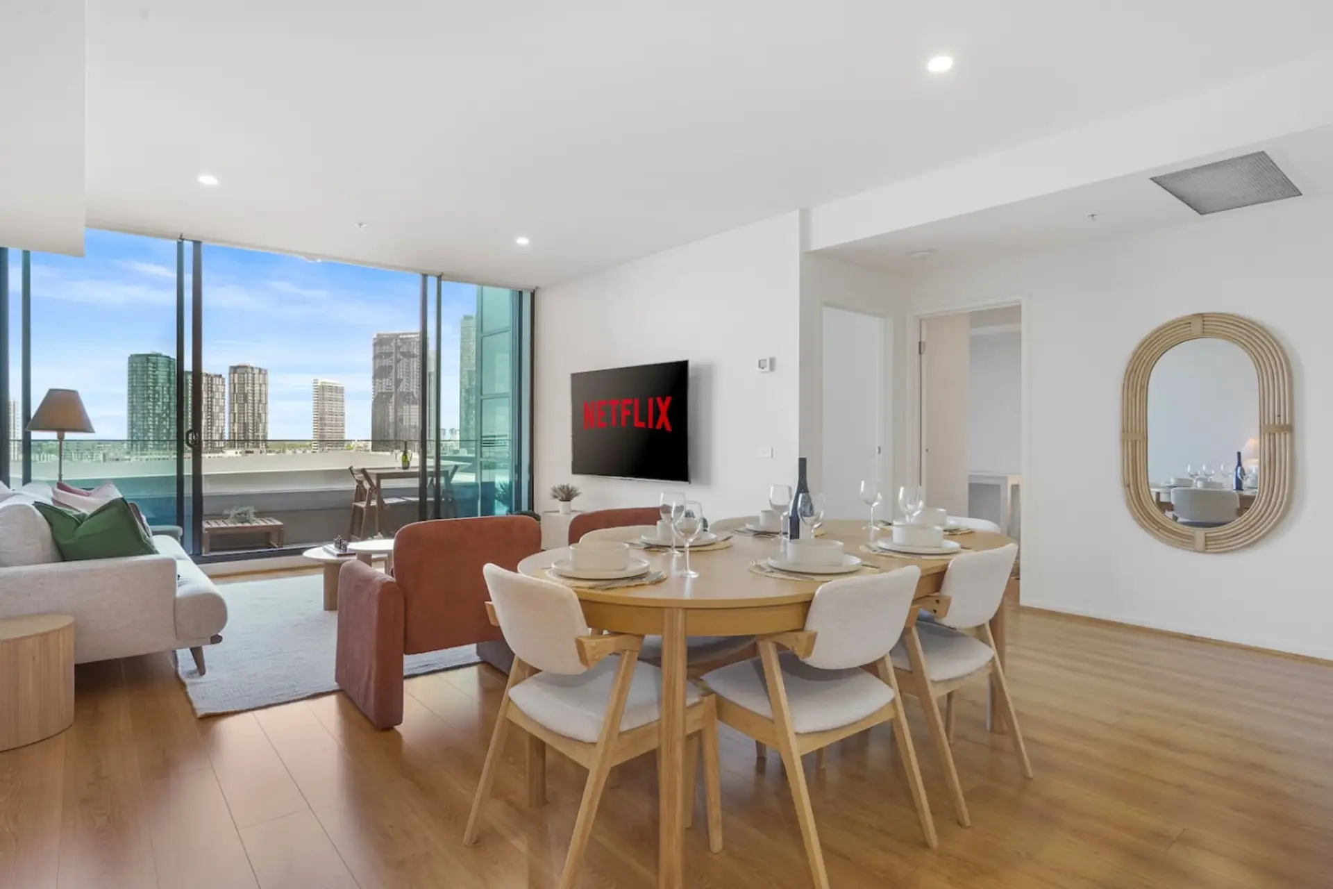 A bright, modern living and dining space with floor to ceiling windows opening to impressive city views, perfect for relaxing, streaming, and enjoying meals together.
