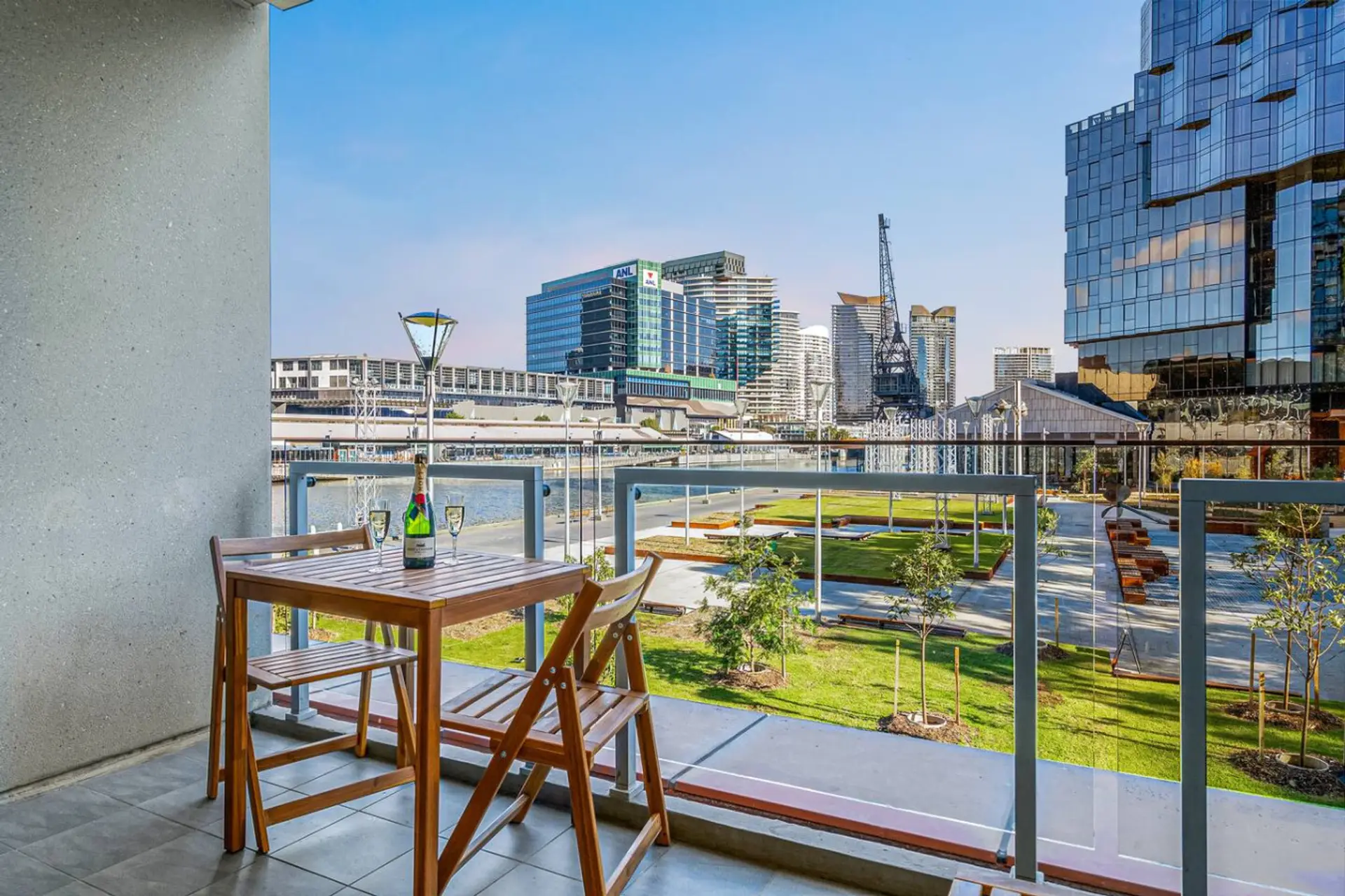 Private balcony with a cosy outdoor dining setup overlooking the river, green open spaces, and Melbourne’s modern skyline, perfect for relaxed mornings or sunset drinks.