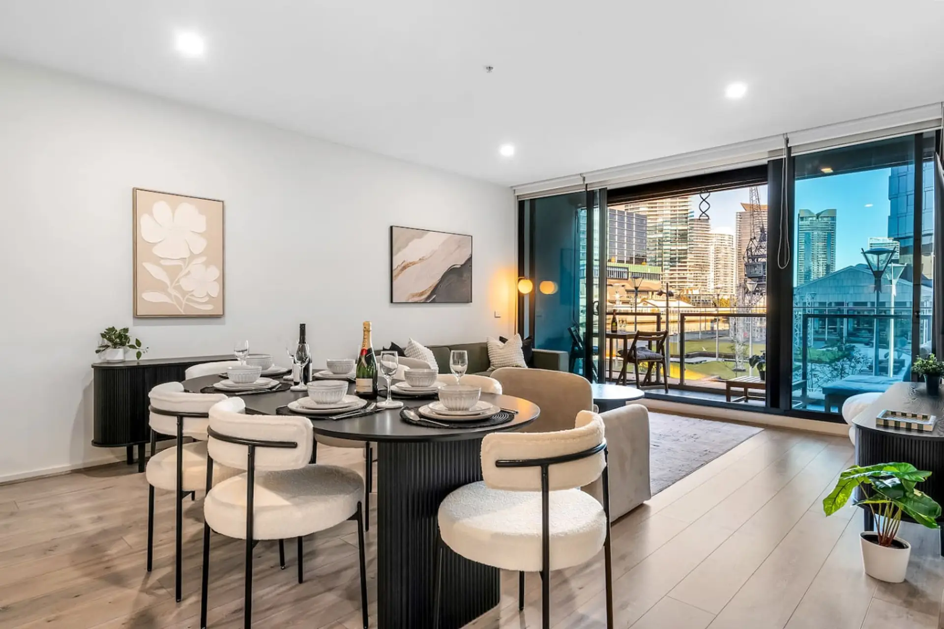 Elegant open plan dining and living area with a modern six seat table, chic decor, and floor to ceiling glass doors opening to a private balcony with beautiful city views. A bright, stylish space for dining and relaxing.
